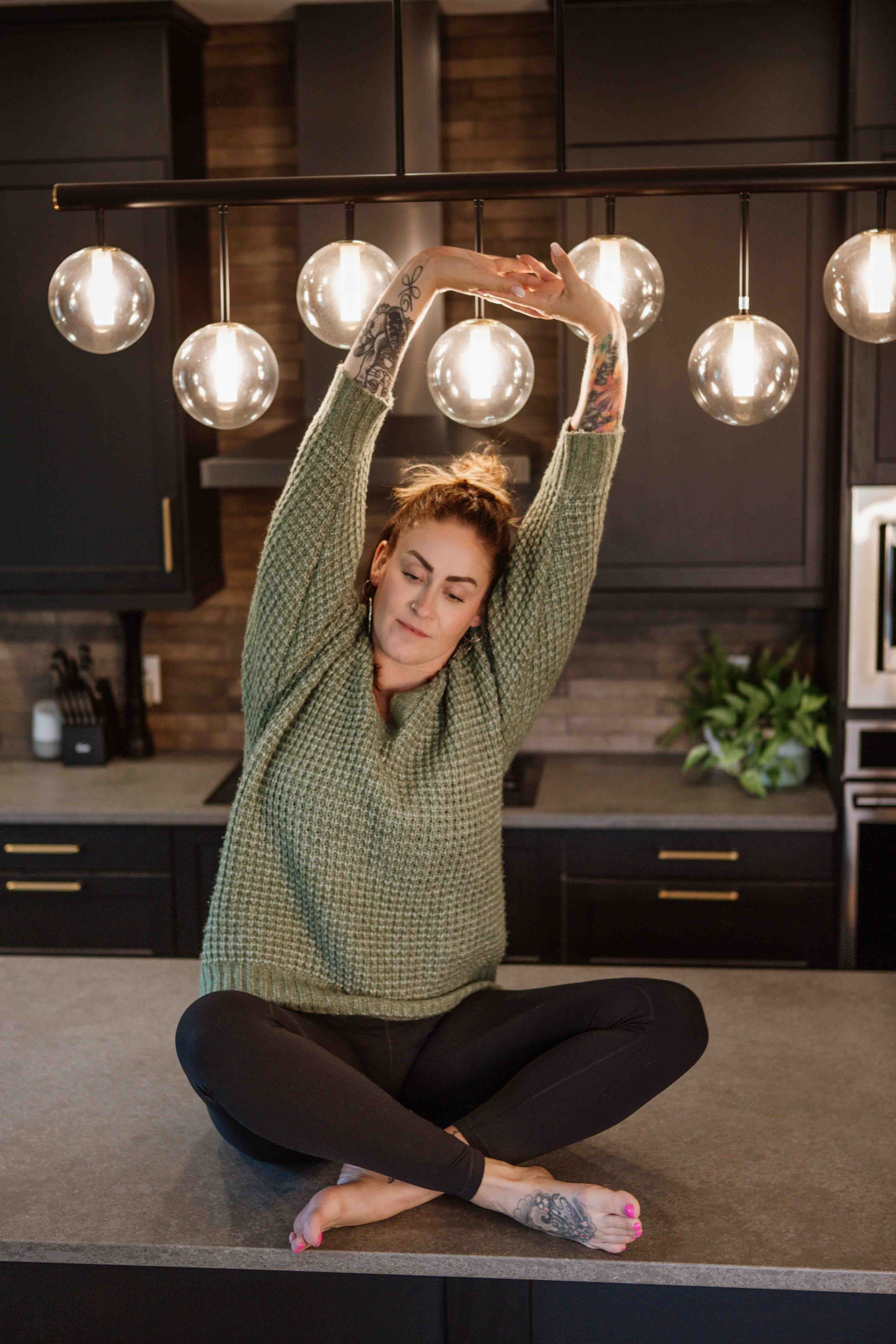 A midlife woman in cozy clothing on a kitchen counter practicing yoga