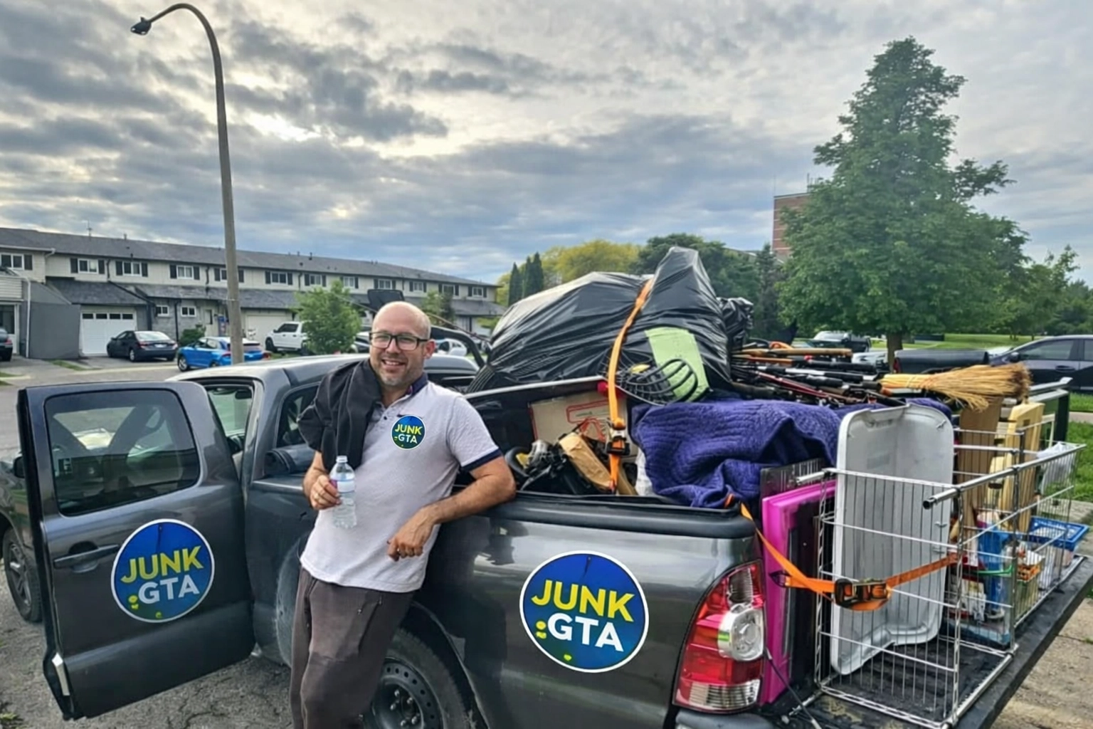 Reliable Junk Removal Simcoe County: Keeping Our Community Clean Roman, owner of Junk GTA, standing by his 2014 Toyota Tacoma loaded with junk for removal in a residential neighborhood.