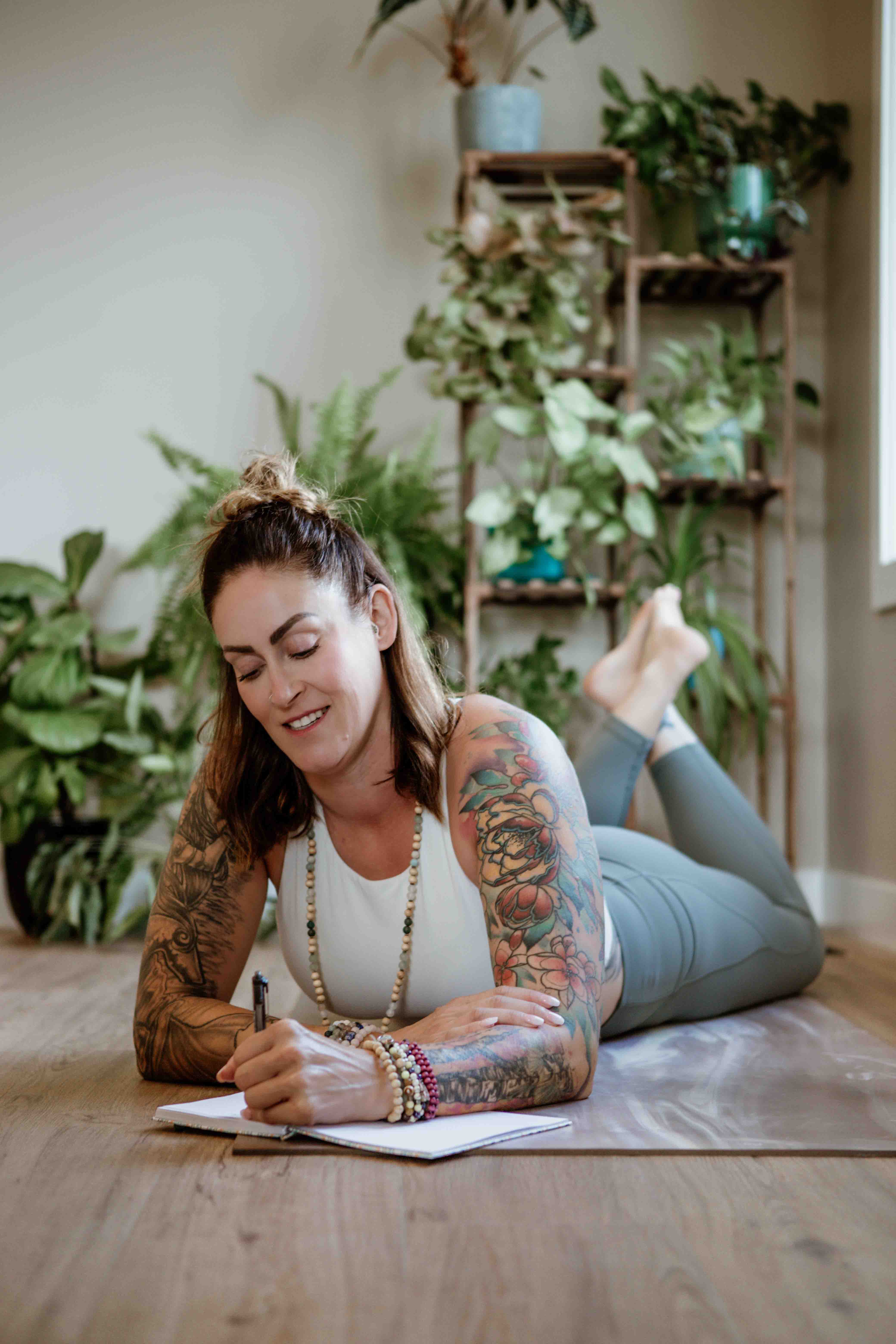 A midlife woman journaling on a yoga mat surrounded by houseplants