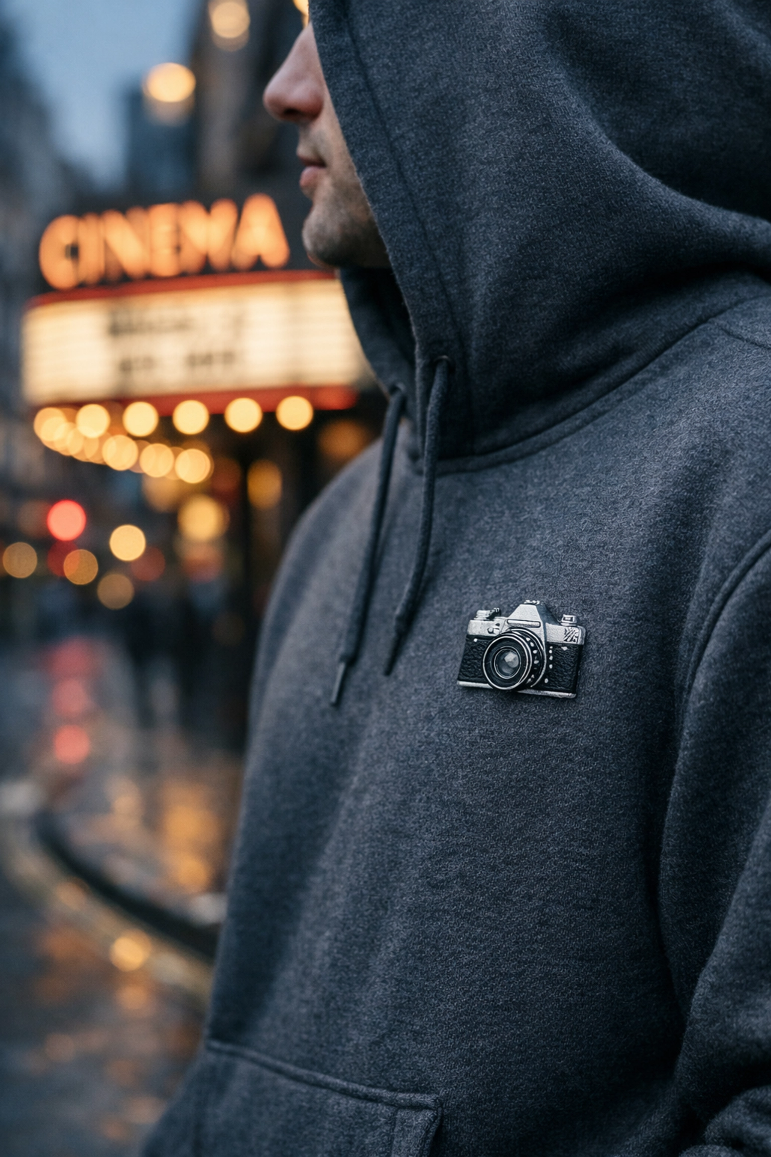 Stylish movie merchandise uk fan wearing a charcoal hoodie with an embroidered vintage film camera.