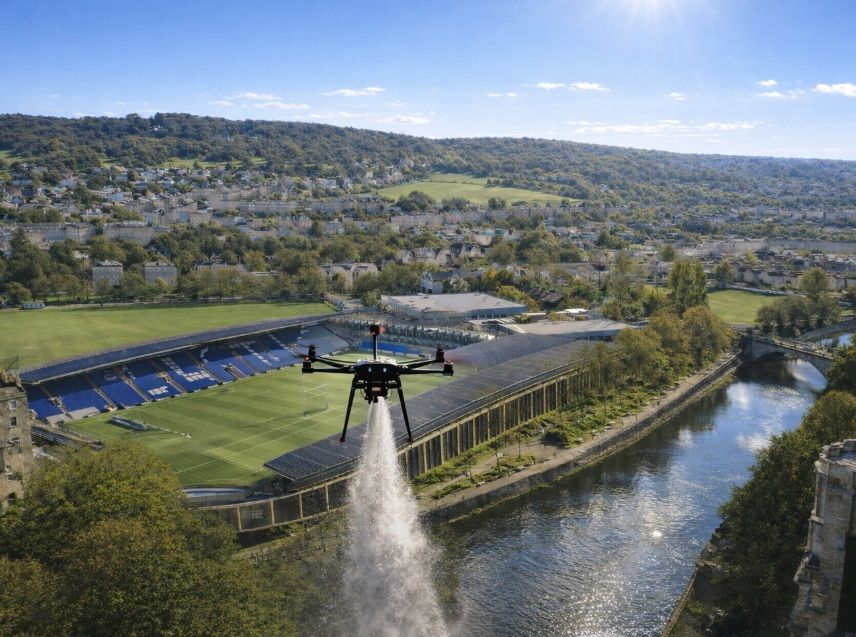 A professional drone releases cremated ashes over a riverside stadium