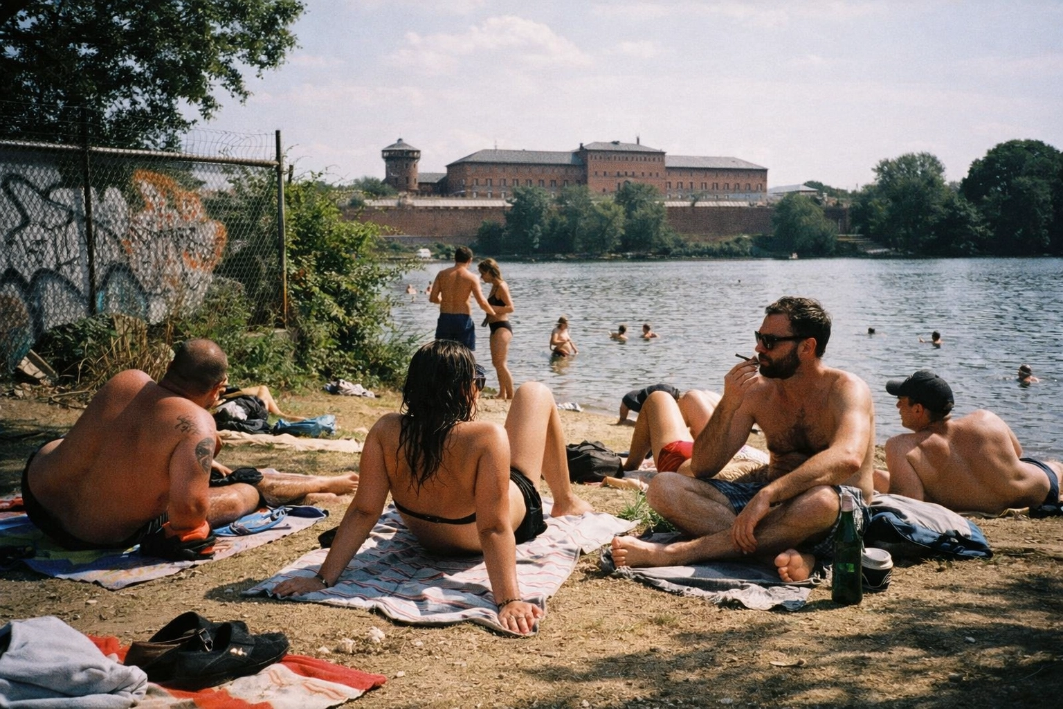 Gritty Plötzensee shoreline in Wedding—urban towels, loud groups, and the prison looming in the background like a quiet threat.