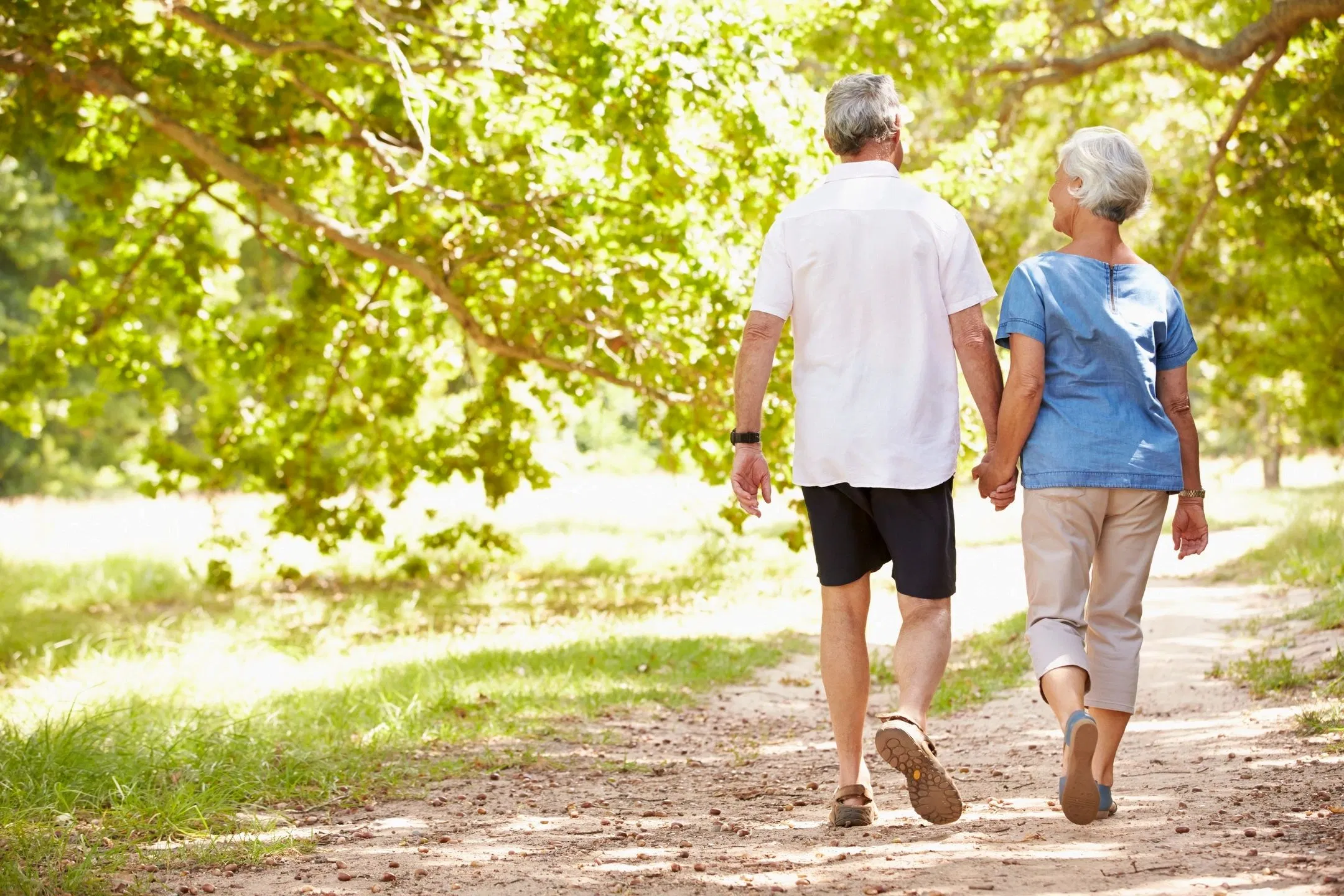 older-couple-walking-sunlit-tree-lined-path.webp