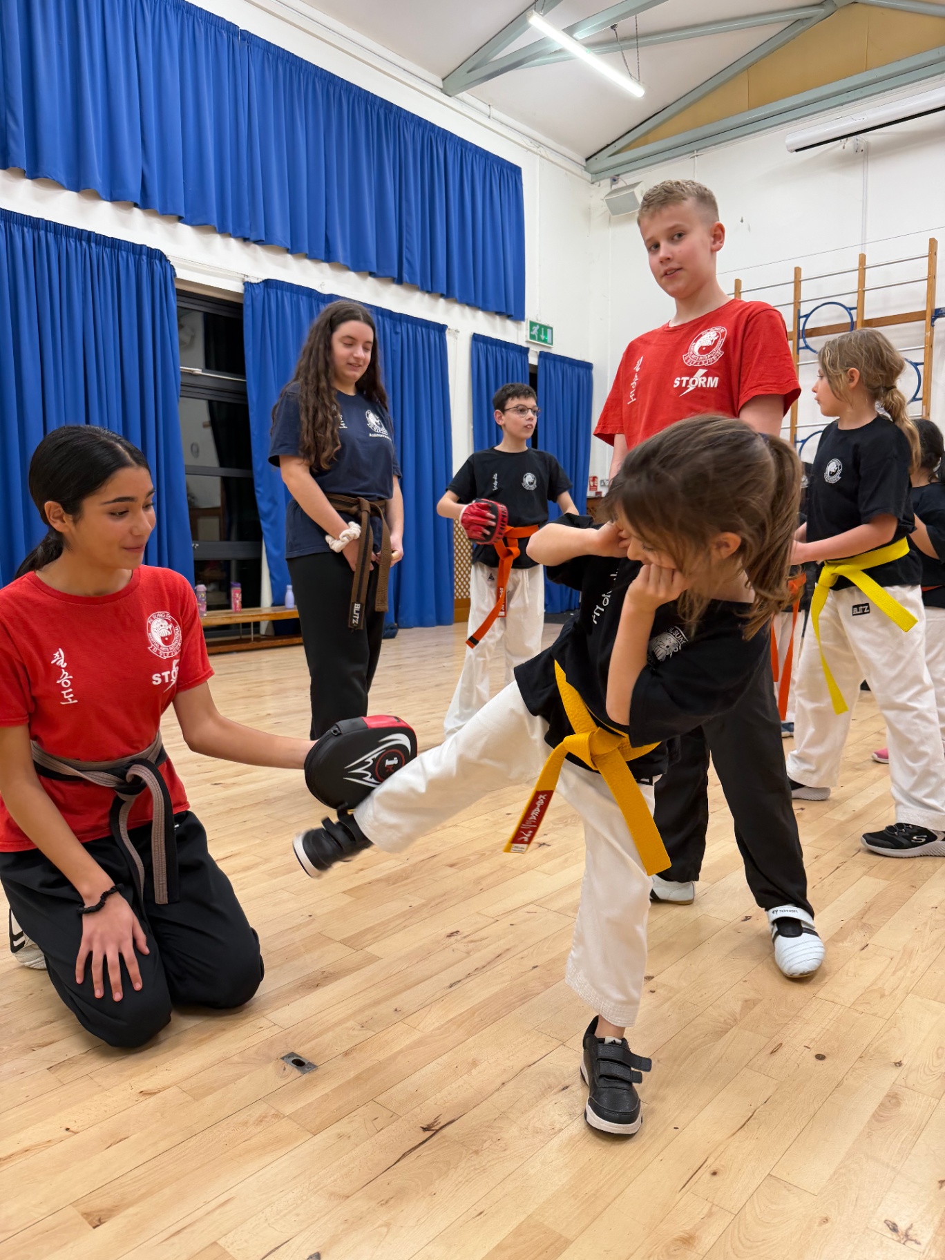 A young instructor holding a target pad for a child practicing a front kick