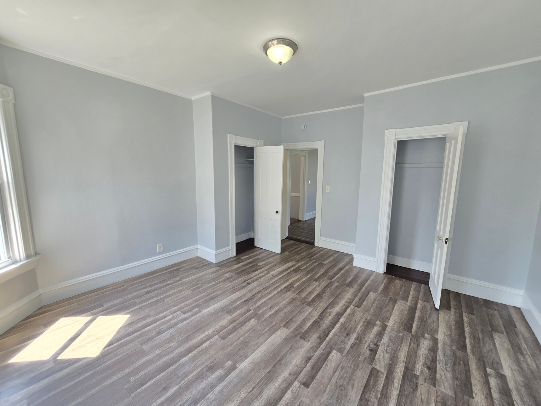 Spacious Renovated Bedroom A freshly renovated bedroom featuring abundant natural light, modern laminate flooring, two closets with white trim, and neutral gray walls. Move-in ready and ideal for residential living in Connecticut.