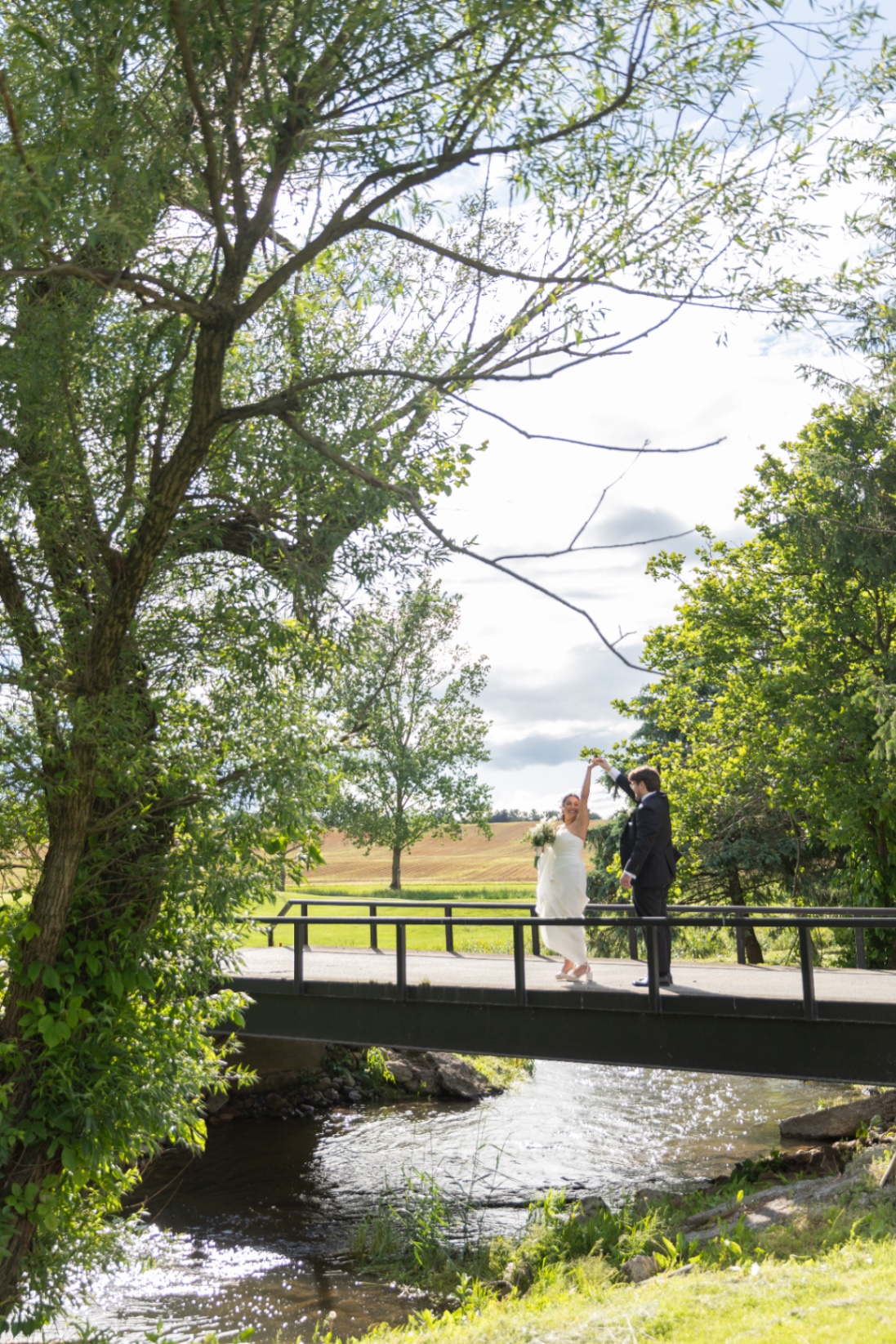 A bride and groom dance together on a small bridge over a stream, full of joy