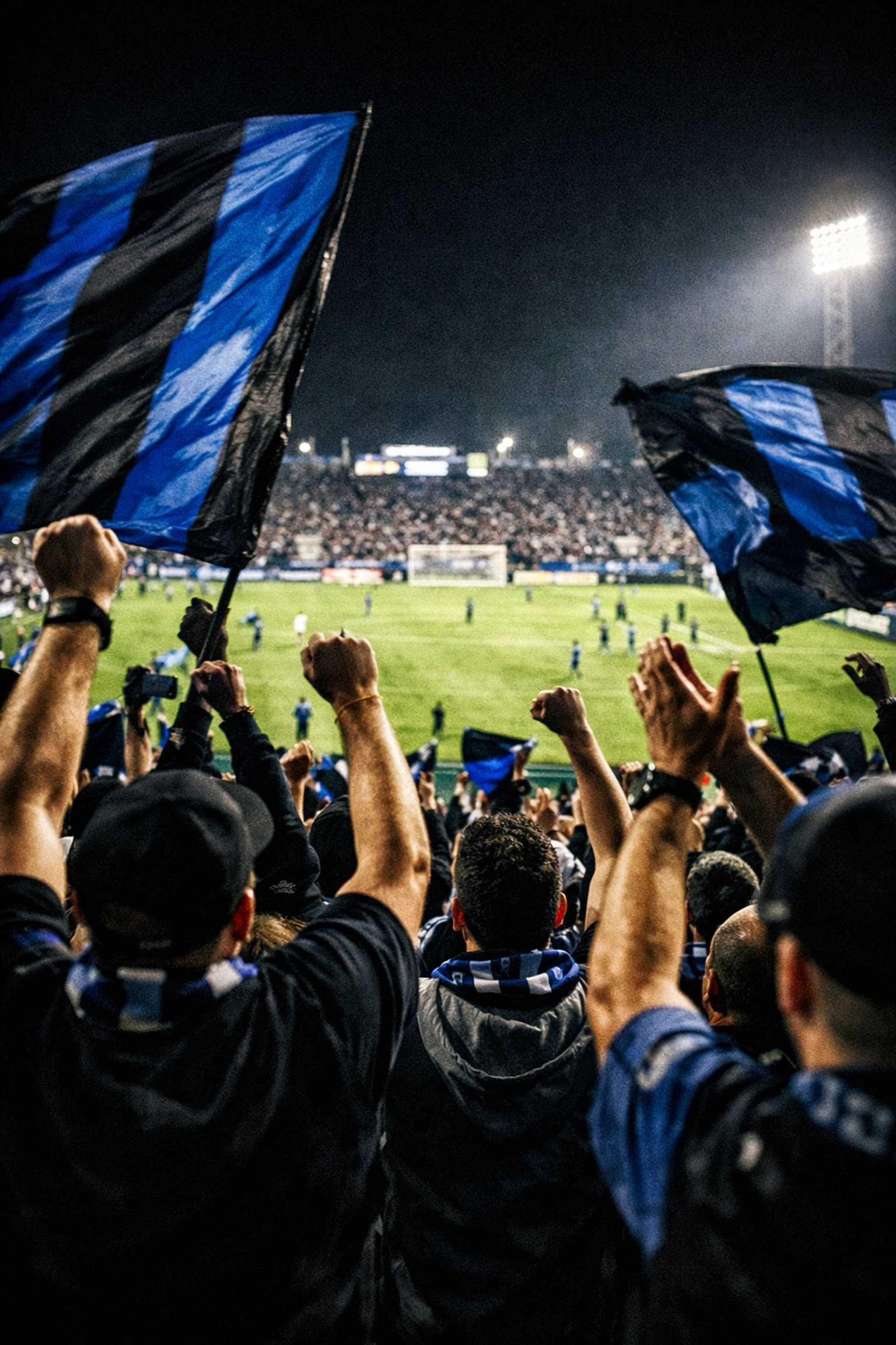 CF Montreal fans cheering and waving blue flags in the supporters' section during a night game at Stade Saputo.