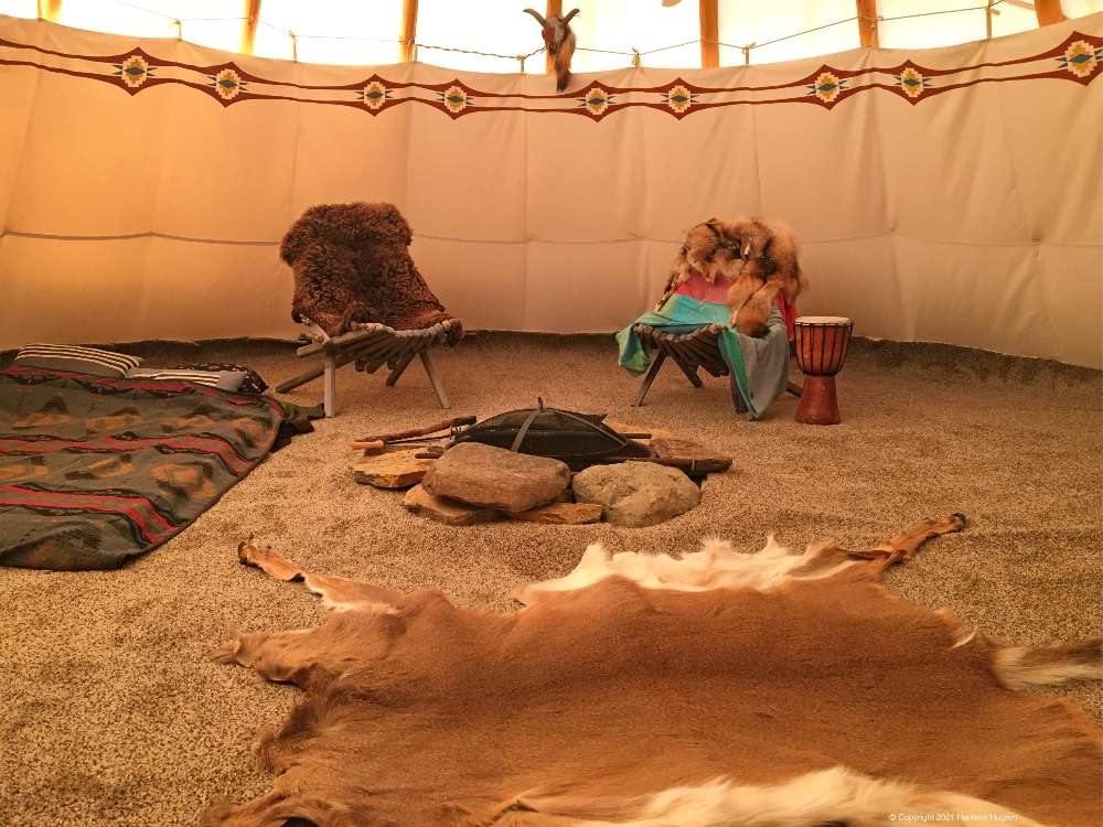 Rustic glamping-style interior with animal hides and a fire pit (representative of the cozy, unplugged gathering feel coming Spring 2026).