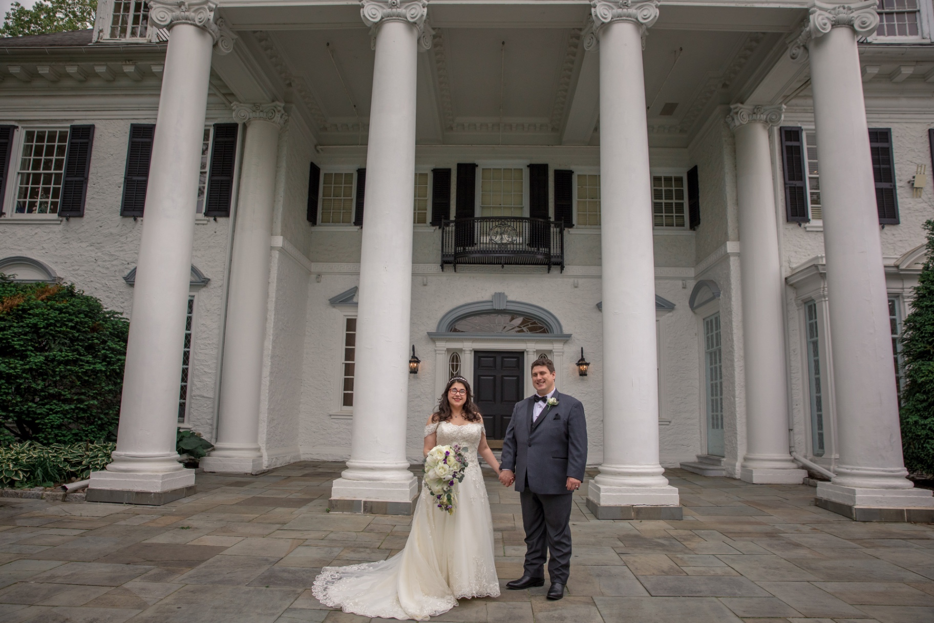 Bride and groom holding hands in front of a grand white mansion with tall columns