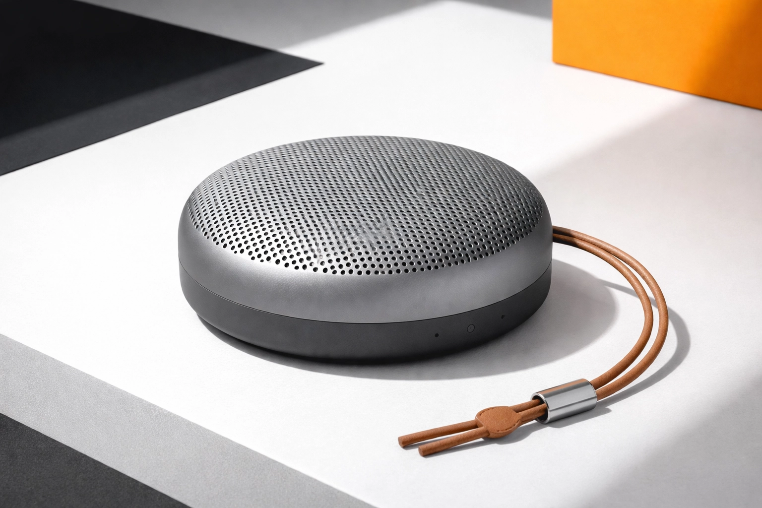 Premium compact portable speaker with a strap on a tabletop, realistic (not hyper-realistic) product photo with bold high-contrast accents.