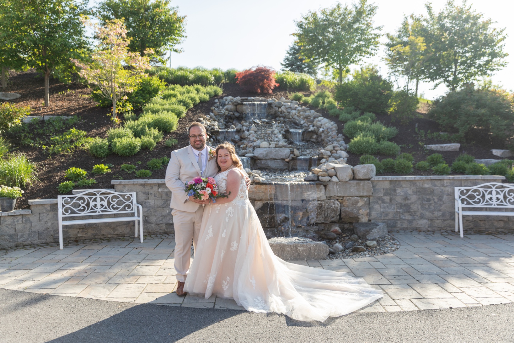 Bride and groom in front of the garden waterfall—sunlit, relaxed, and joyfully present