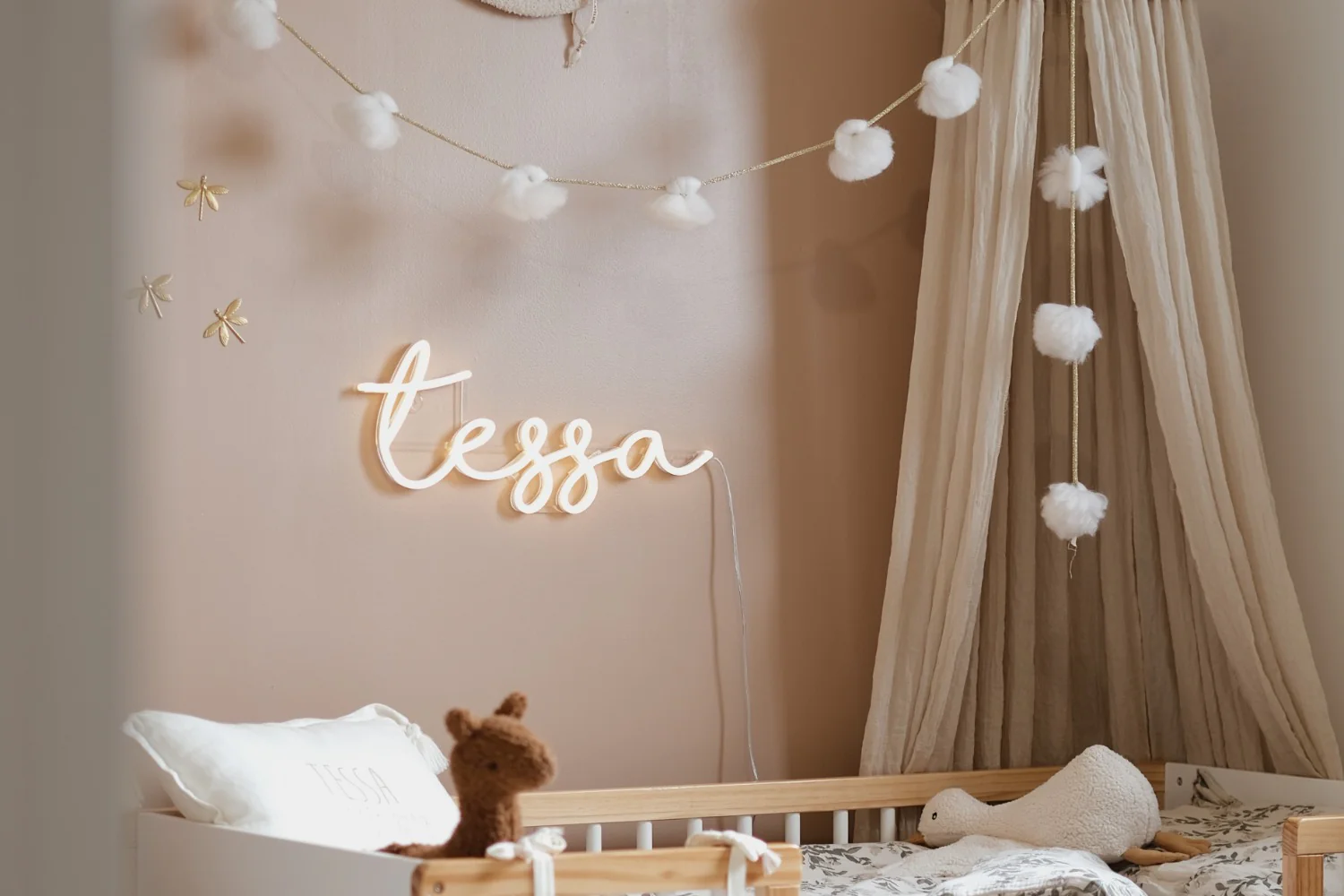 Custom LED neon sign in script font, mounted above a child's bed in a softly decorated nursery