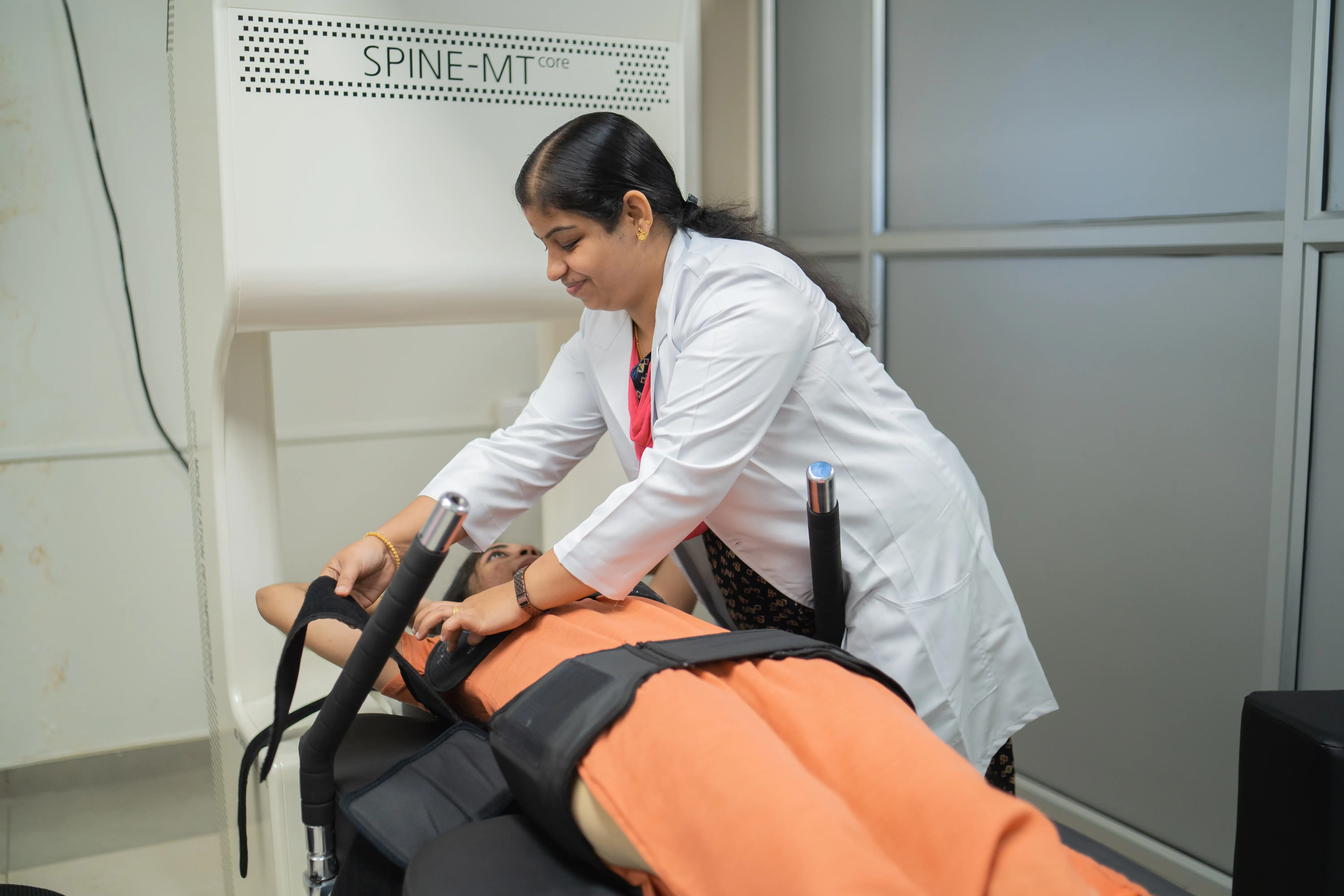 A physiotherapist fits a patient with safety straps before starting a session on the advanced SPINE-MT core spinal decompression machine