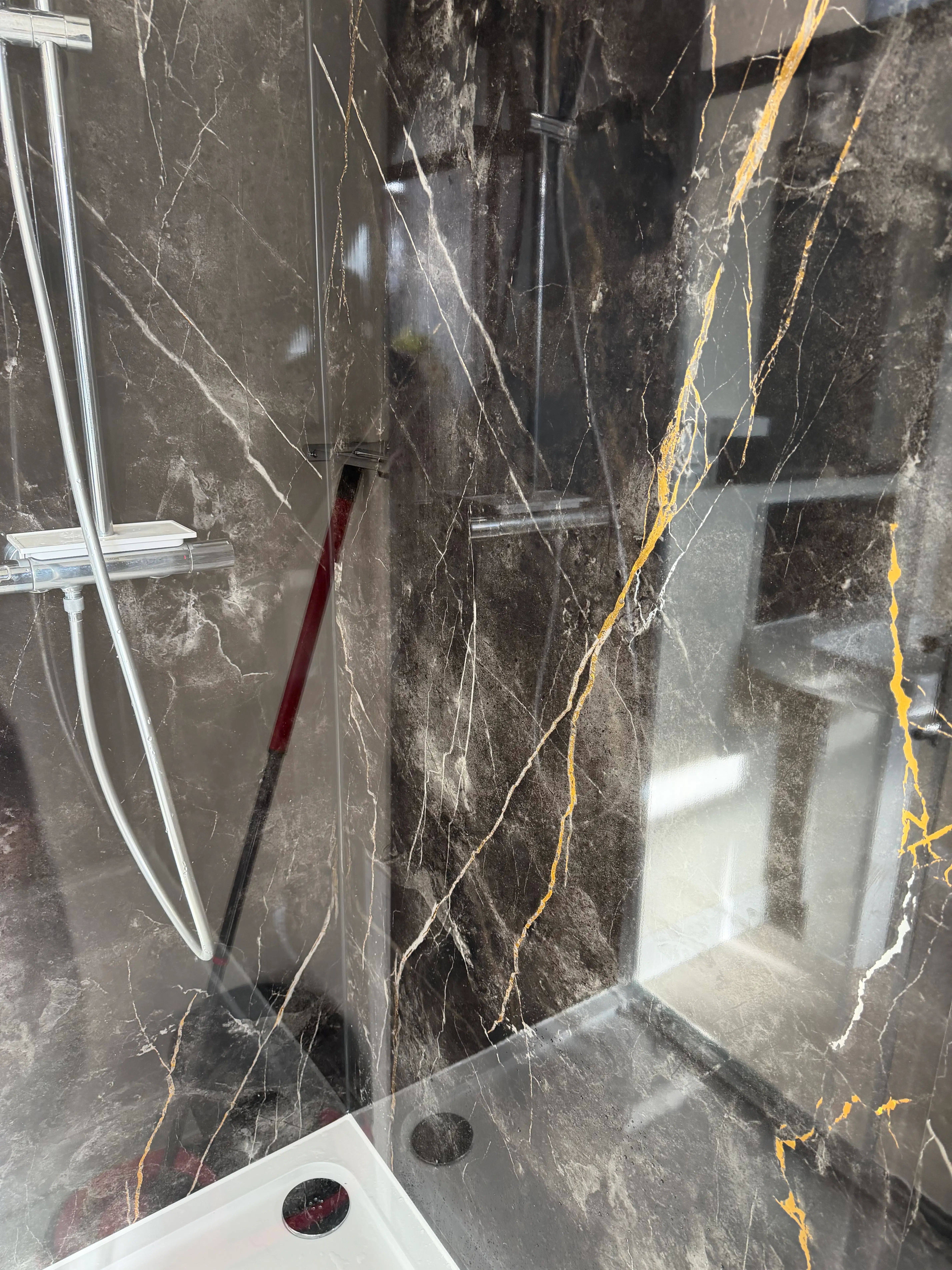 Newly installed modern shower with dark marble-effect wall panels and chrome fixtures