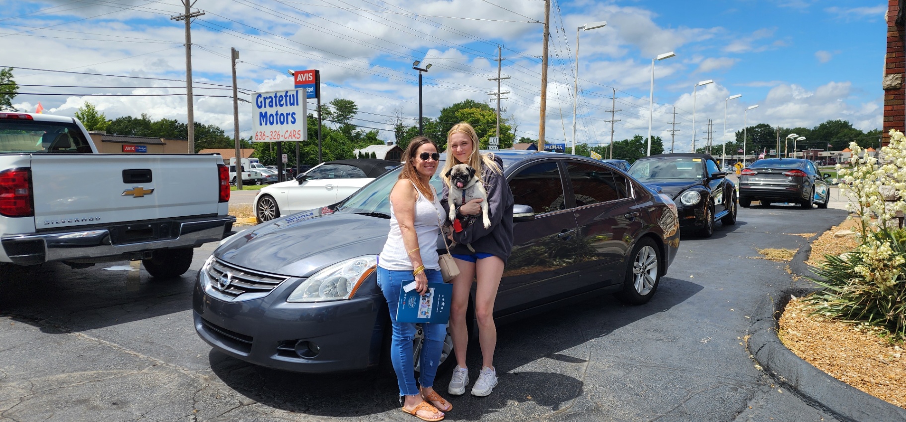 Two customers with their dog and new dark gray sedan at Grateful Motors