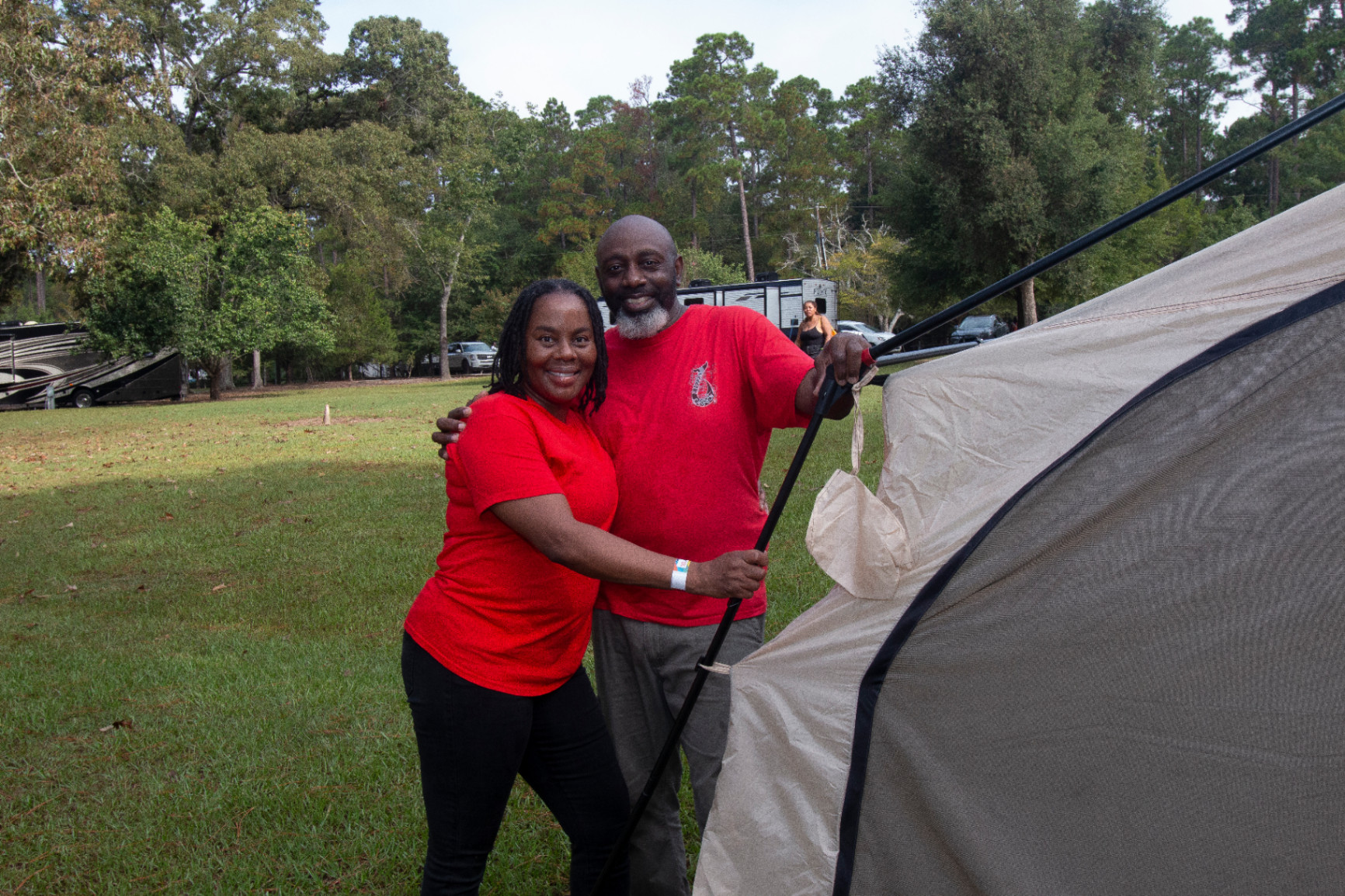 Two adults in matching red shirts are smiling and setting up a tent