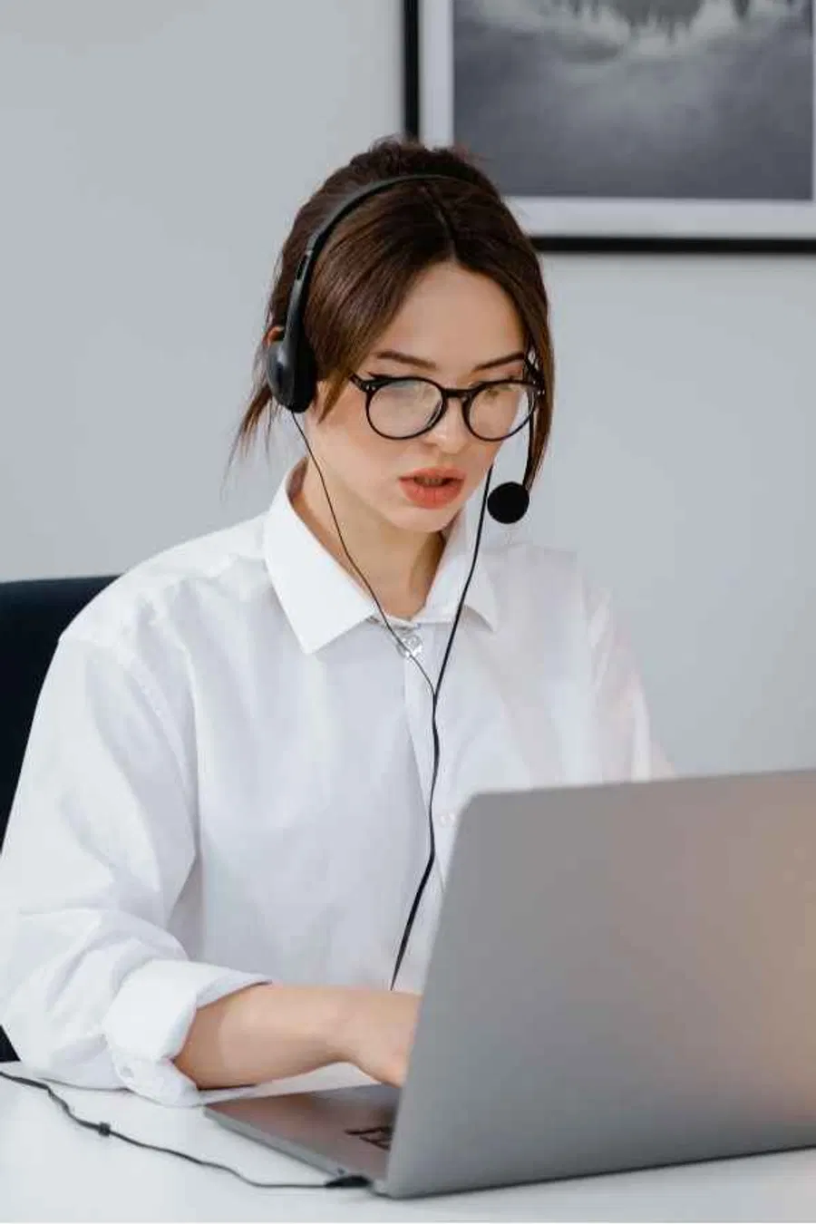 A remote virtual assistant in a professional setting, wearing a headset and working efficiently on a laptop