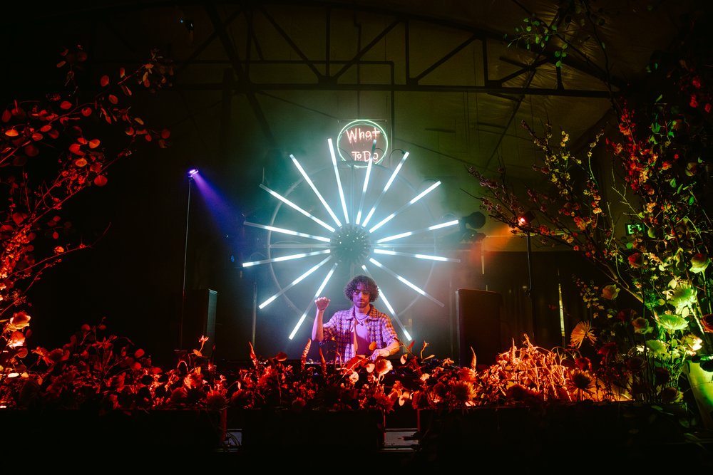 DJ performing on stage at The Foundry SF with vibrant lighting and floral arrangements