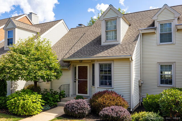 Well-maintained Townhouse Exterior Beige vinyl siding, two front-facing dormer windows, landscaped shrubs, and paved walkway to entrance; sunny weather accentuates clean roof and curb appeal in a Connecticut residential neighborhood.