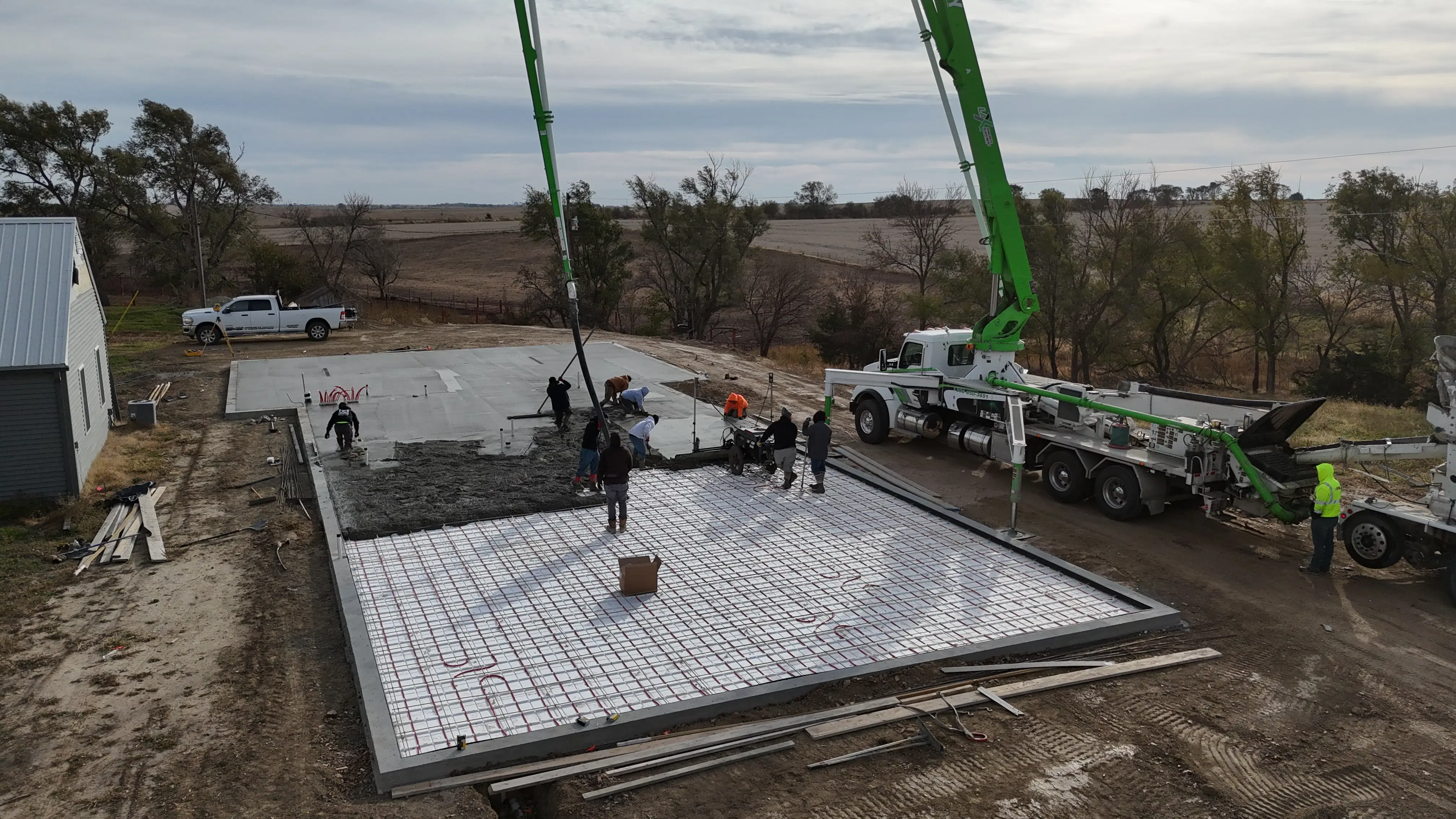 Large team using boom pump trucks to pour and level concrete for a commercial slab foundation with visible rebar.