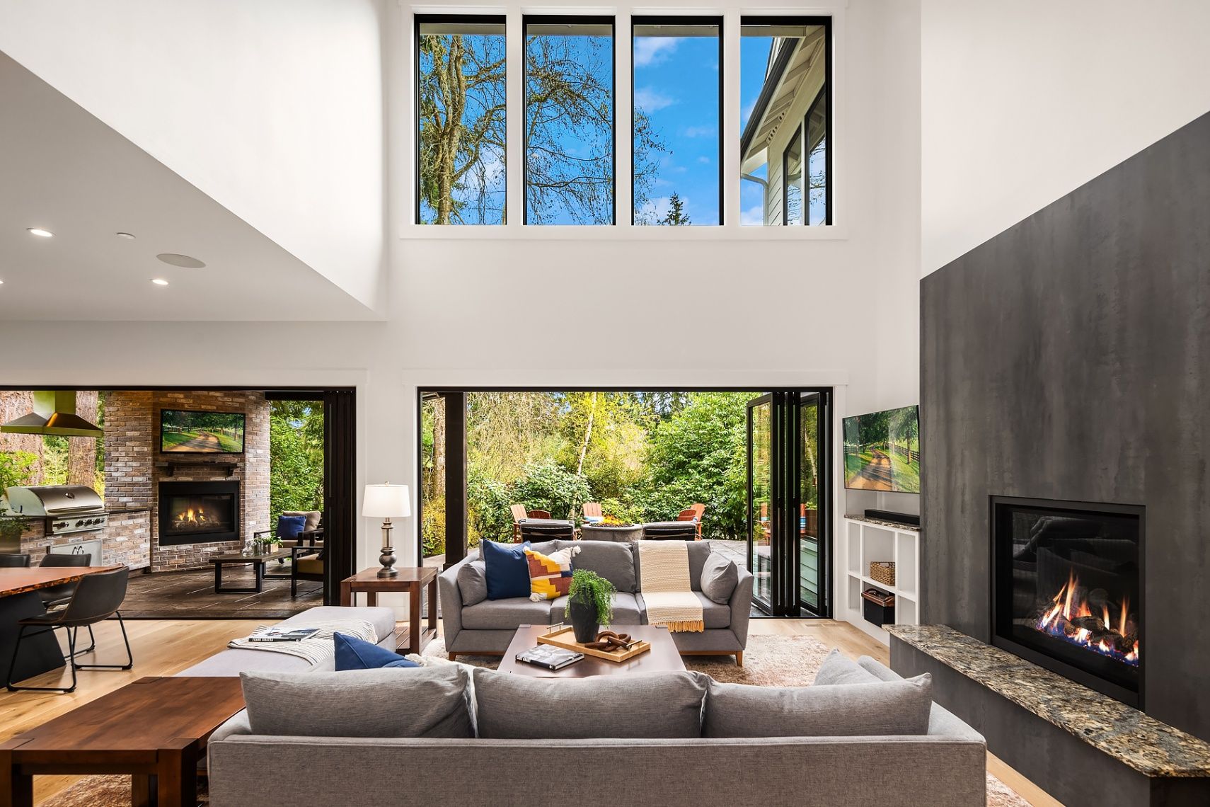 Modern living room with high ceilings and seamless indoor-outdoor flow to a patio with fireplace/kitchen