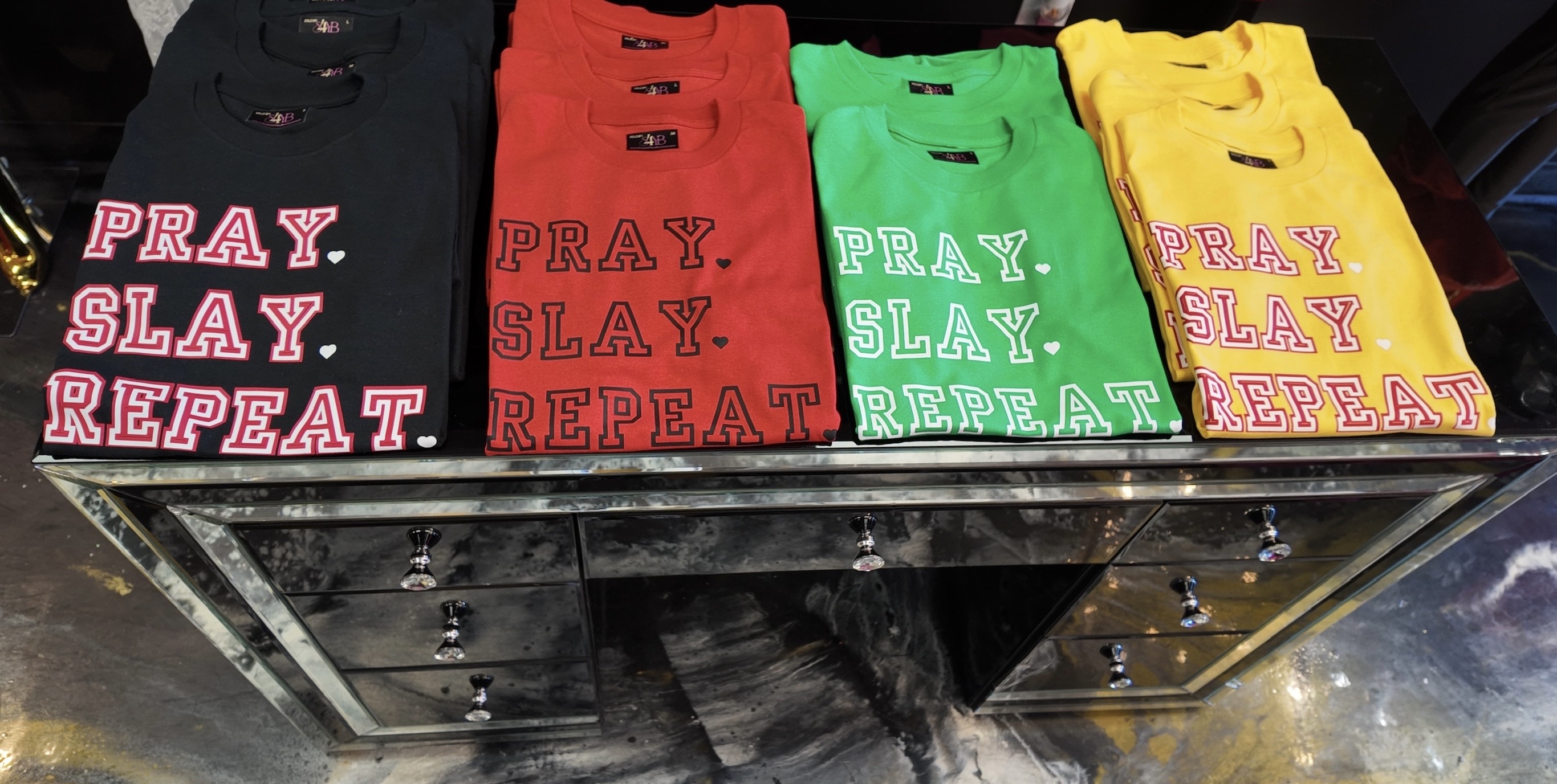A colorful display of the new Pray Slay Repeat t-shirt collection in black, red, green, and yellow.