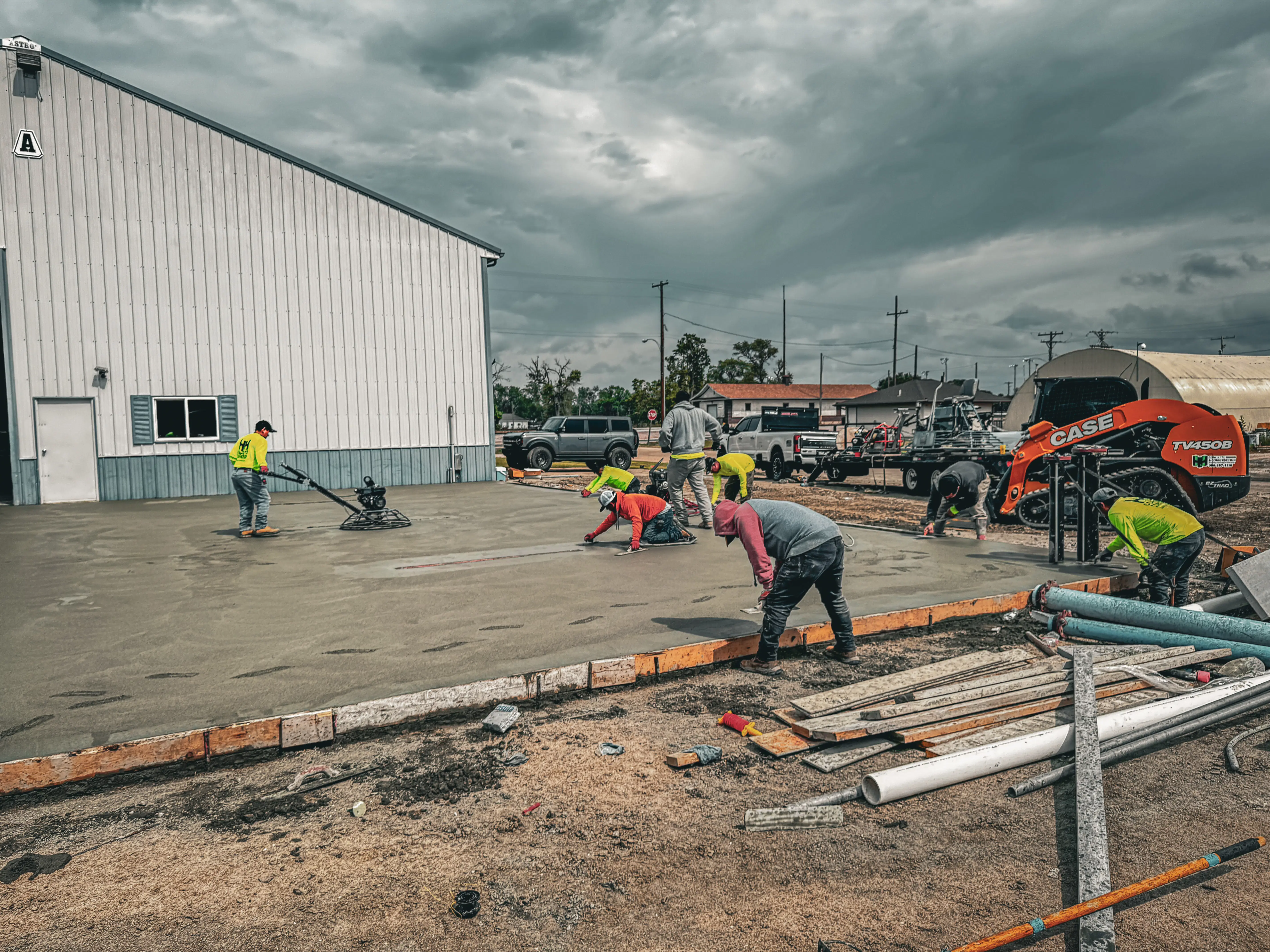 Team members smoothing and finishing freshly poured concrete outside a commercial building