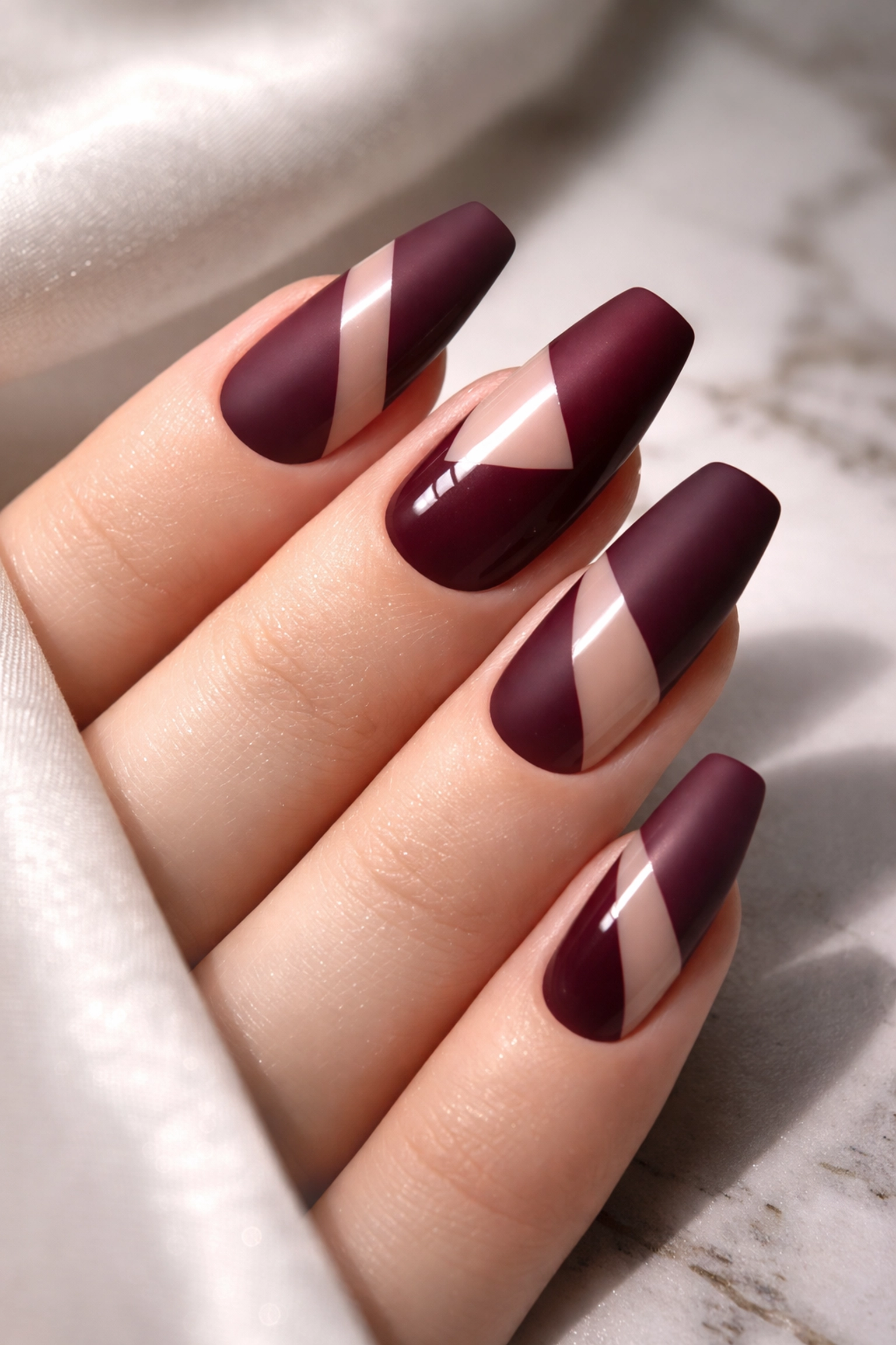 Matte-on-glossy fashion nails with geometric negative space patterns in deep burgundy