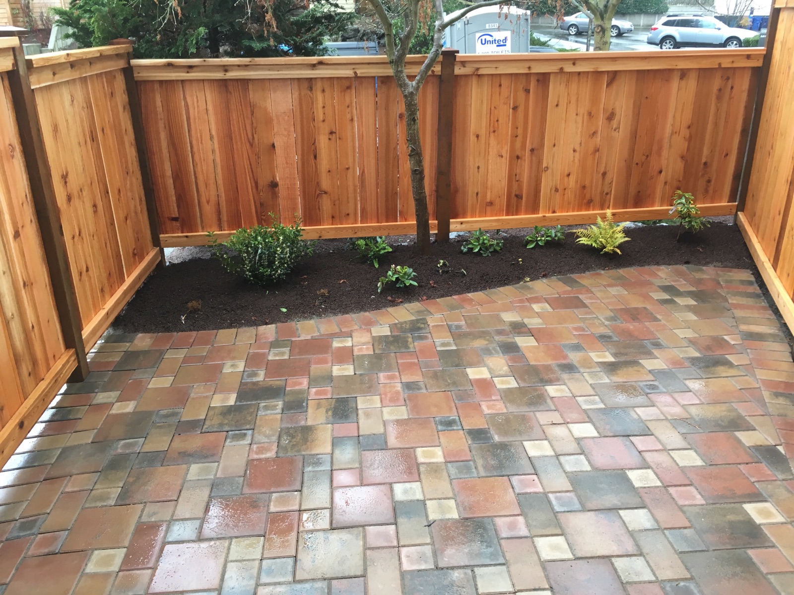 Multi-color paver patio with landscaping and wood fence
