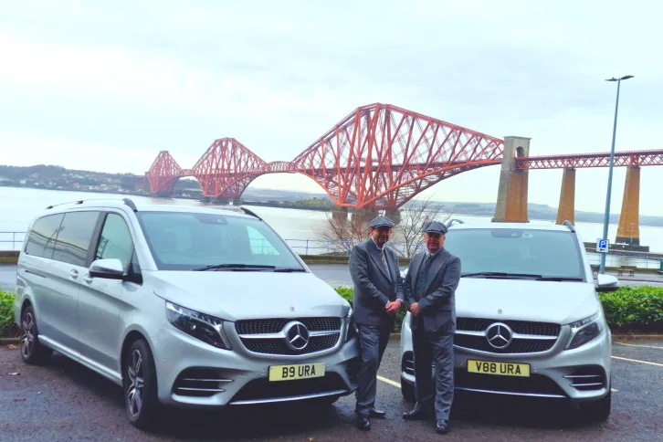Two Aura Journeys chauffeurs in matching suits and hats stand beside luxury Mercedes-Benz vehicles with bespoke number plates