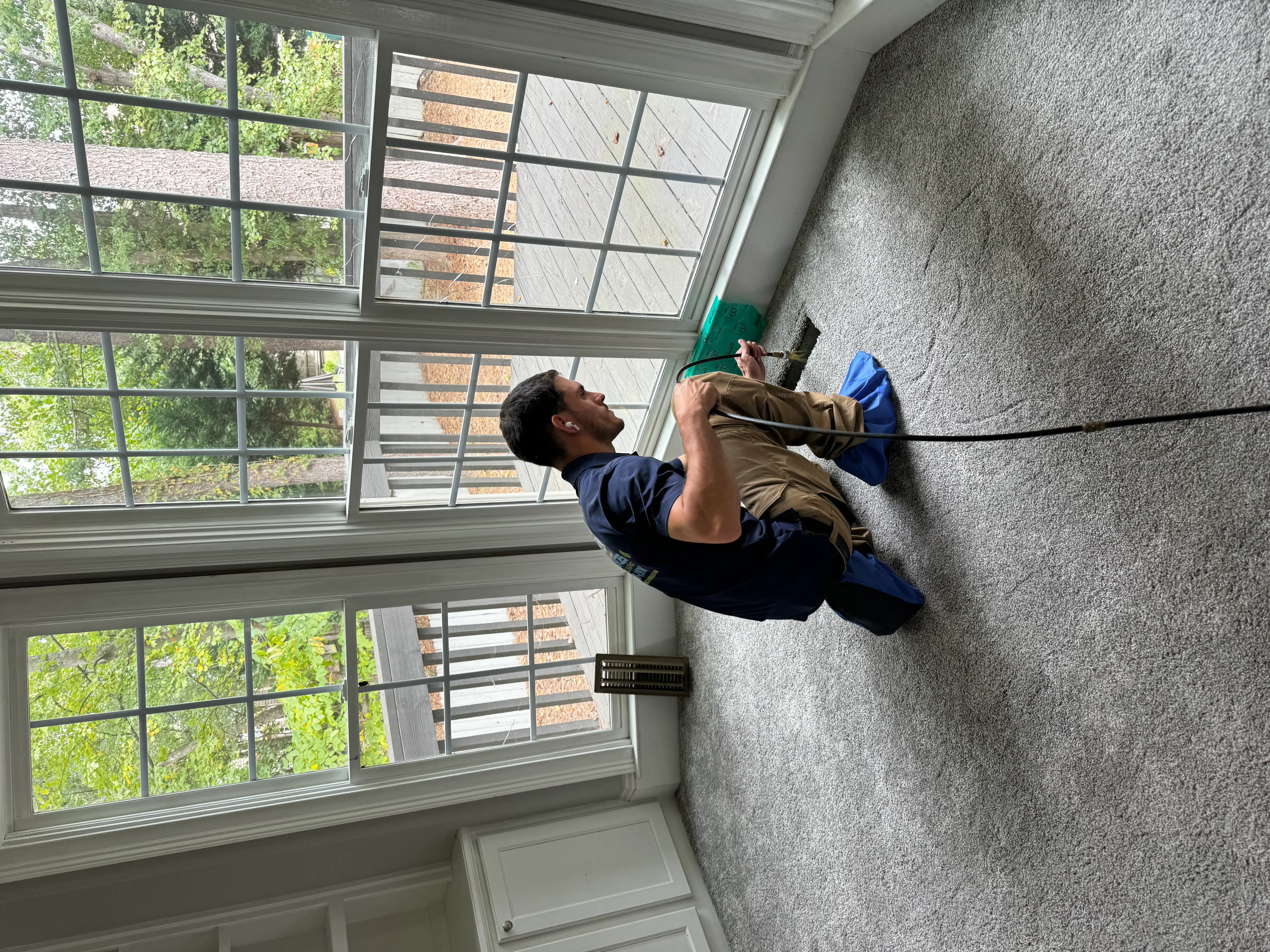 A technician is using a rotary brush tool to clean inside a floor air vent