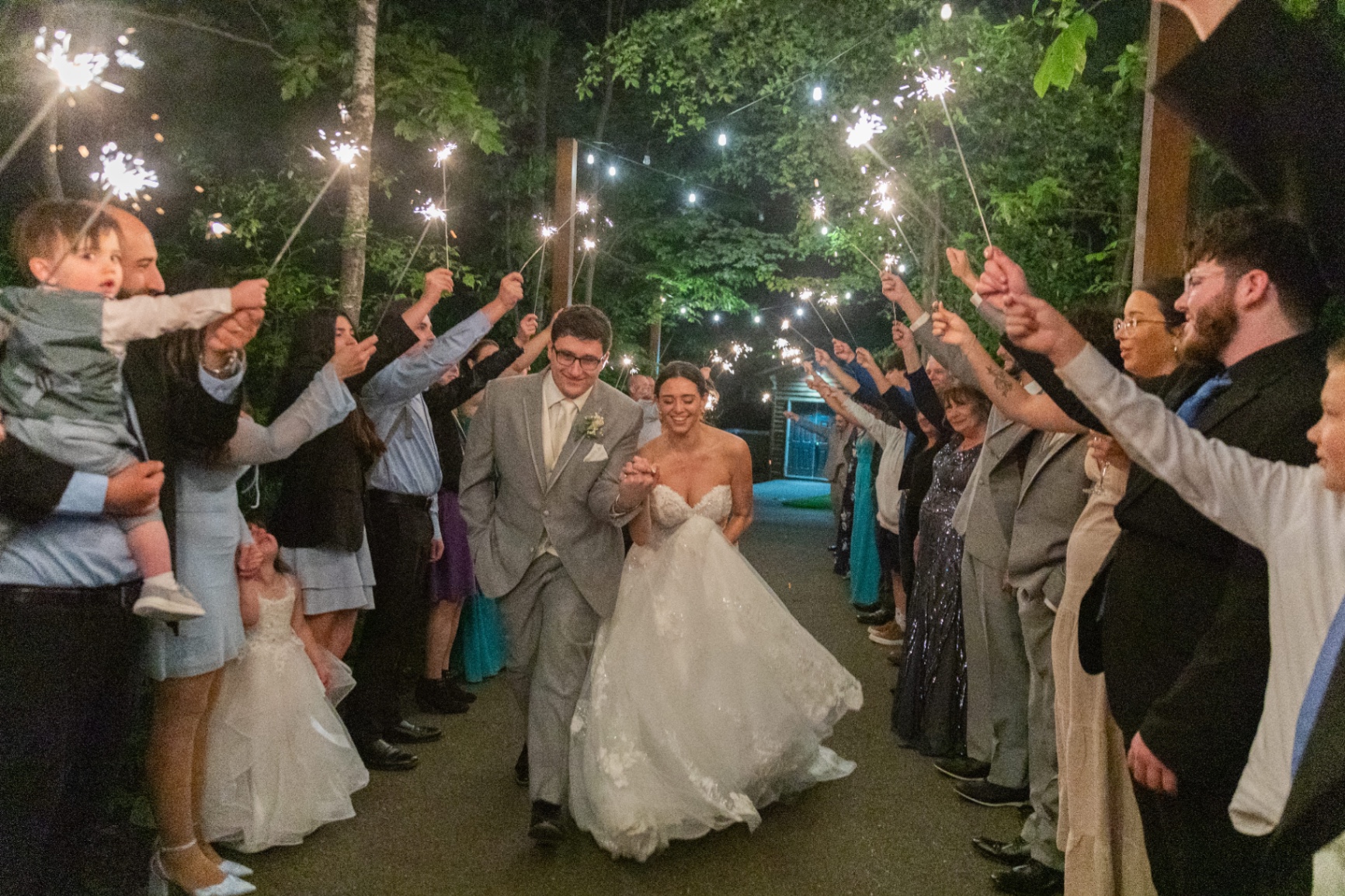 Bride and groom walk hand-in-hand down a sparkler-lit path