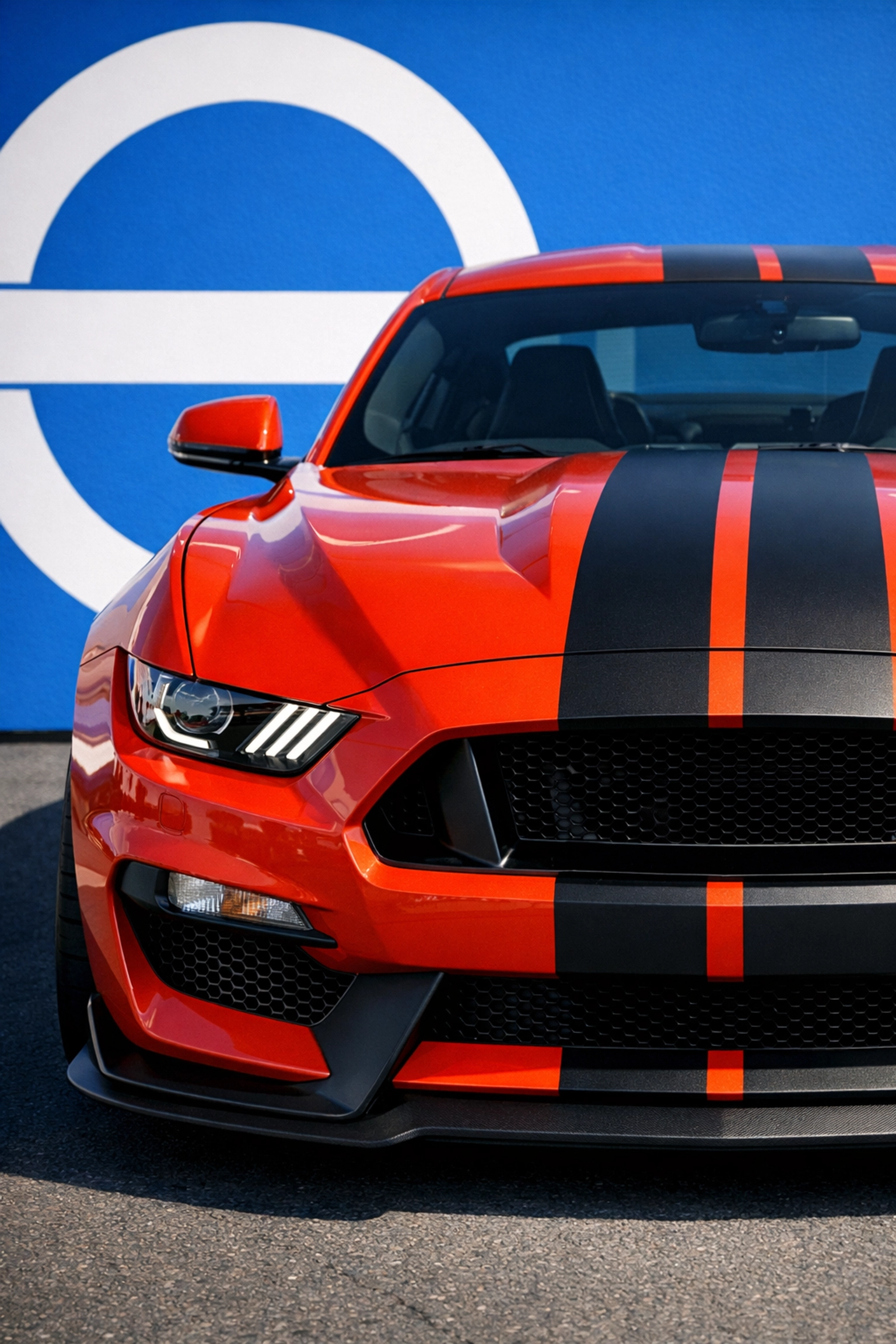 Red performance car with black racing car stripes stickers on the hood against a blue background.