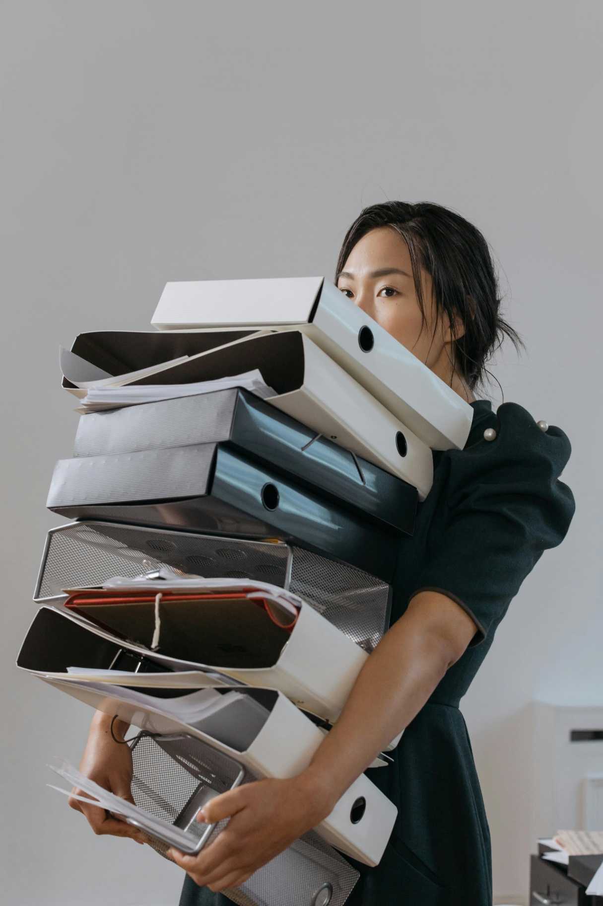 A professional struggles to carry an overwhelming stack of binders and documents