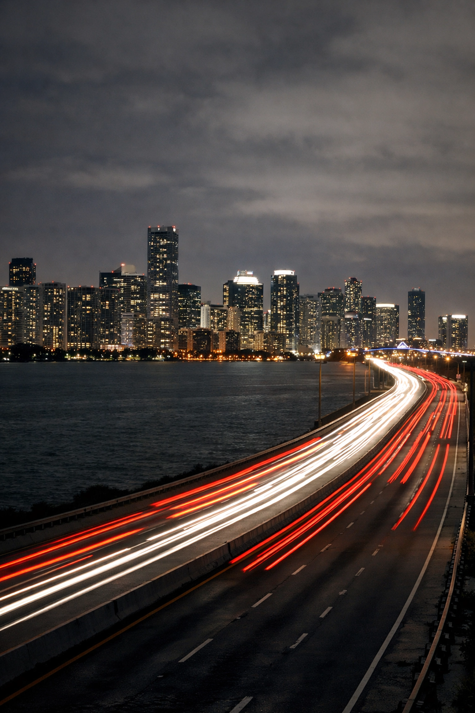 Dramatic light trails from cars on the Rickenbacker Causeway with the glowing Miami skyline at night.