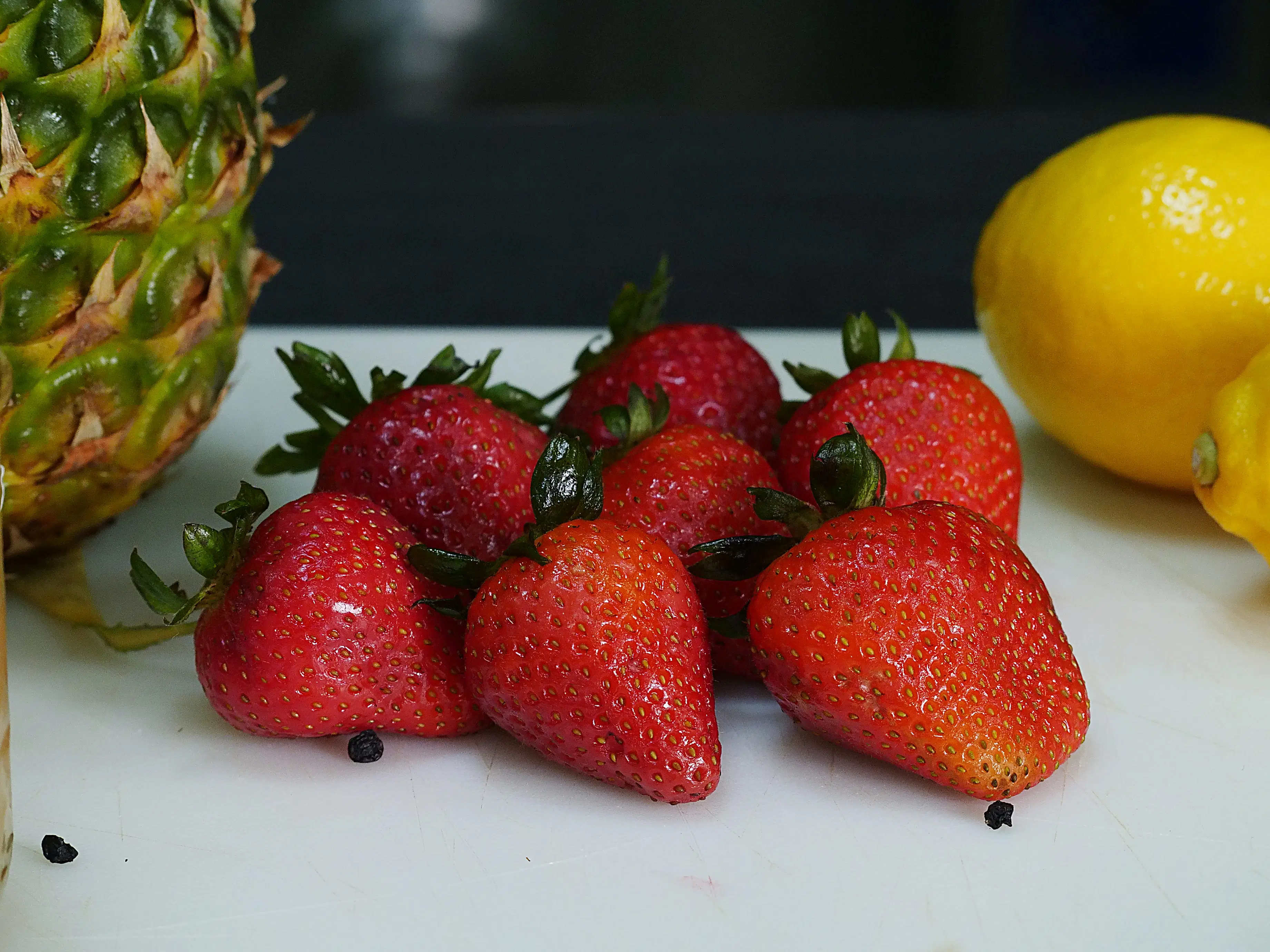 A vibrant assortment of fresh ingredients used for Sea Moss Gel flavors, including strawberries, lemons, blueberries, elderberries, mango, raw gold sea moss, and dried leaves