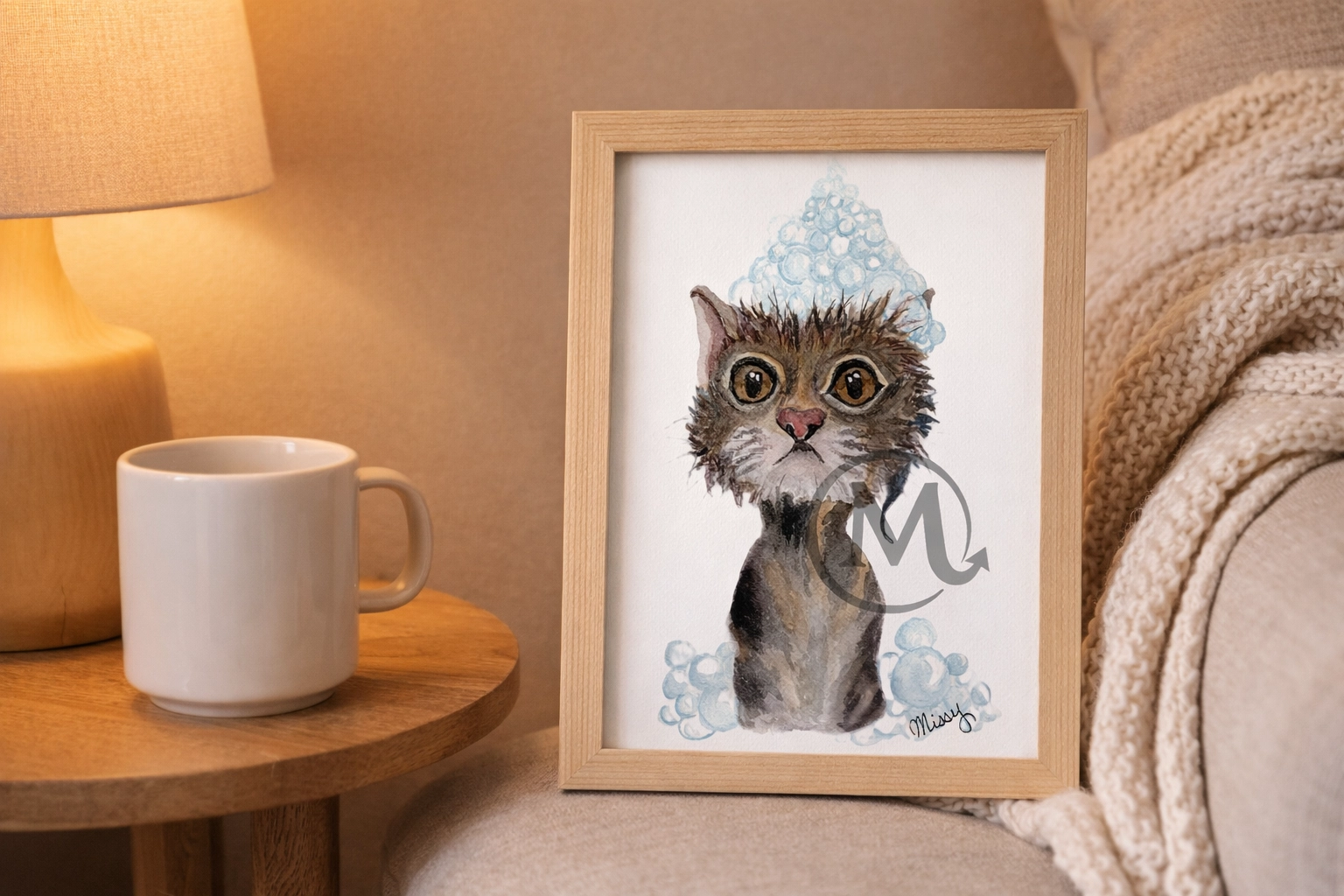 Lifestyle mockup of Missy’s signed tabby kitten watercolor print framed in a cozy living room nook