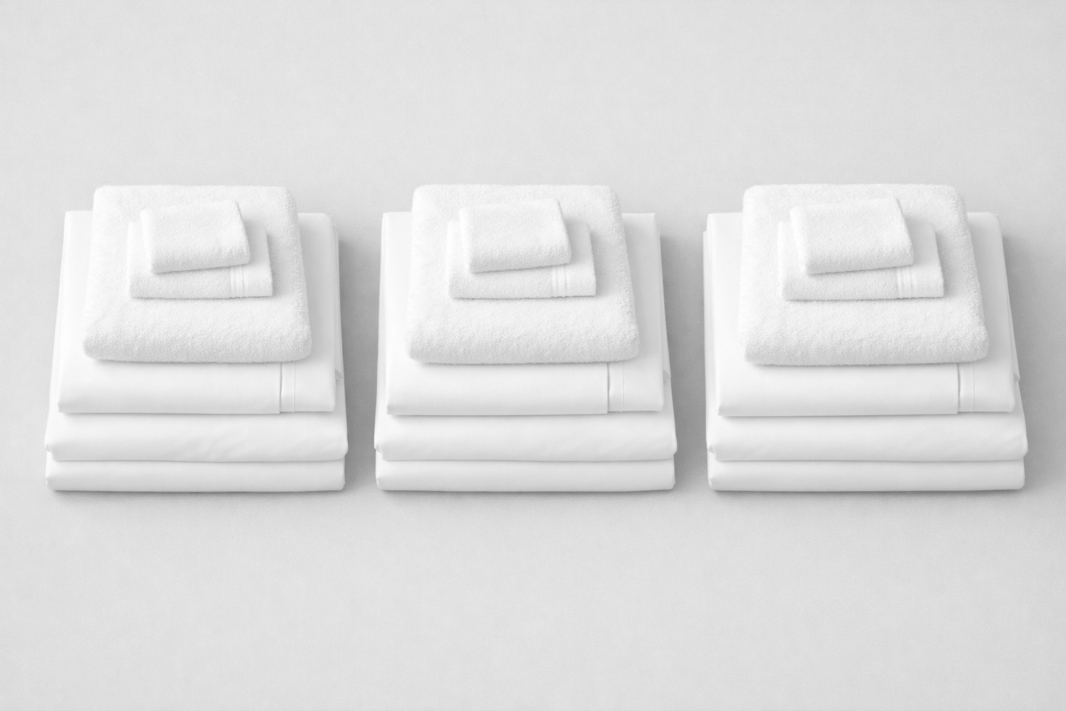 Three sets of folded white linens and towels for apartment turnover efficiency