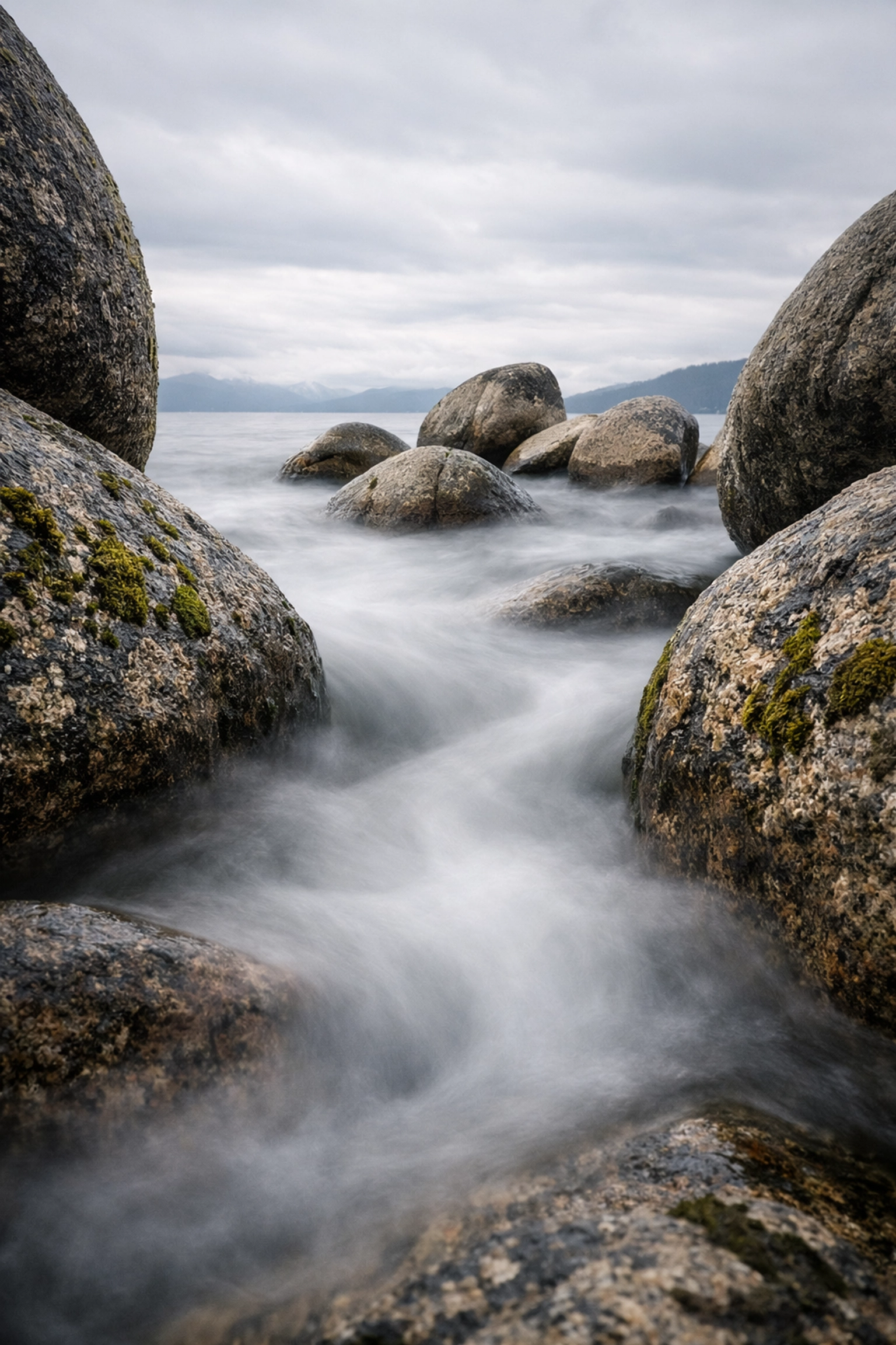 Low-angle long exposure of water swirling around granite boulders at Sand Harbor in Lake Tahoe.
