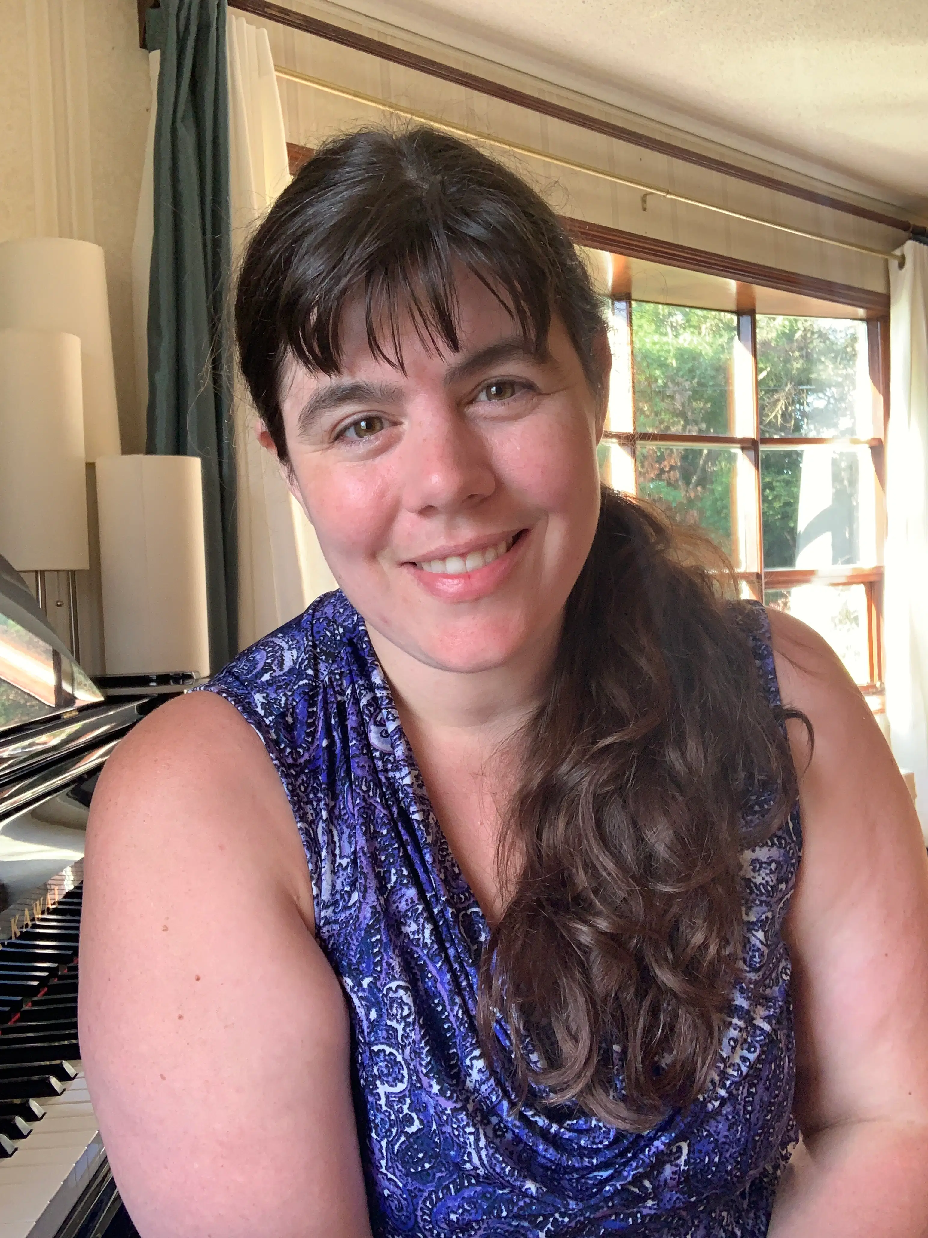 A friendly piano instructor at AM Music Academy sits beside a grand piano in a bright, welcoming studio