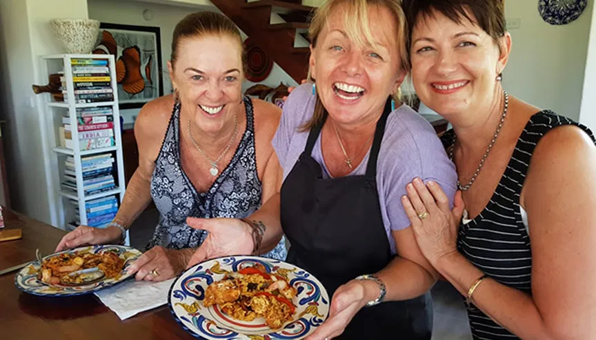 Three happy women holding plates of food they made in a class