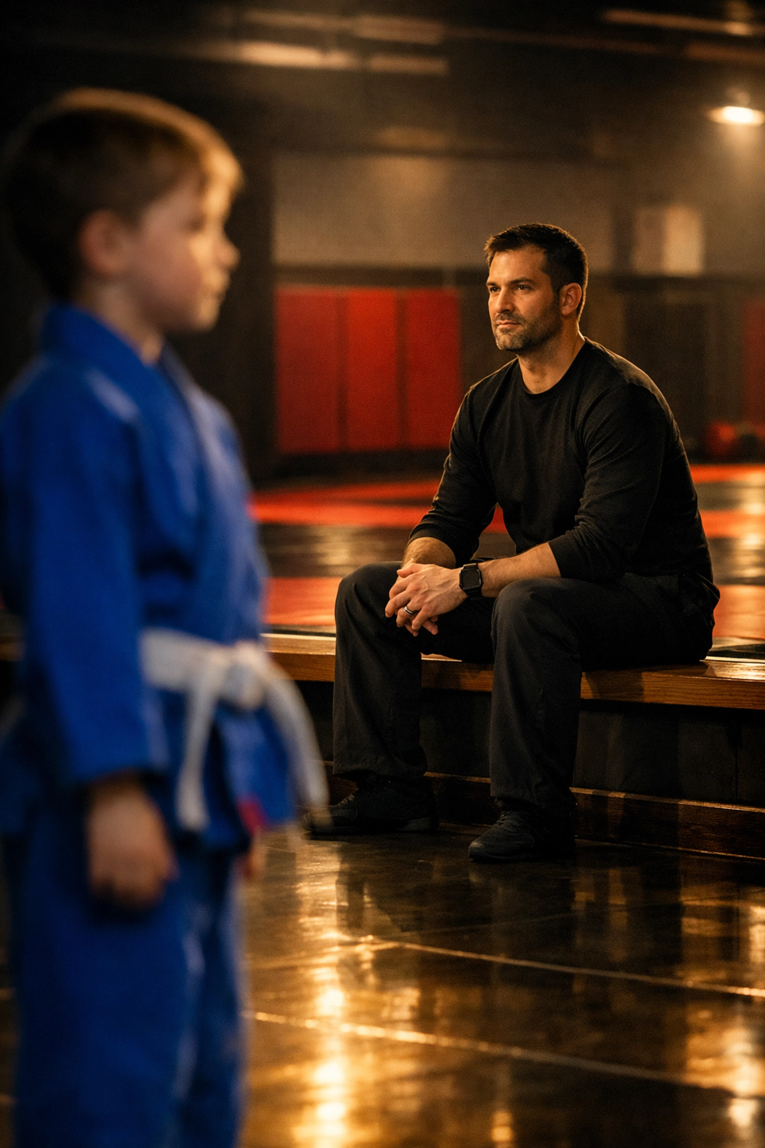 Father modeling discipline and respect from the sidelines during a children's martial arts class in a dojo.