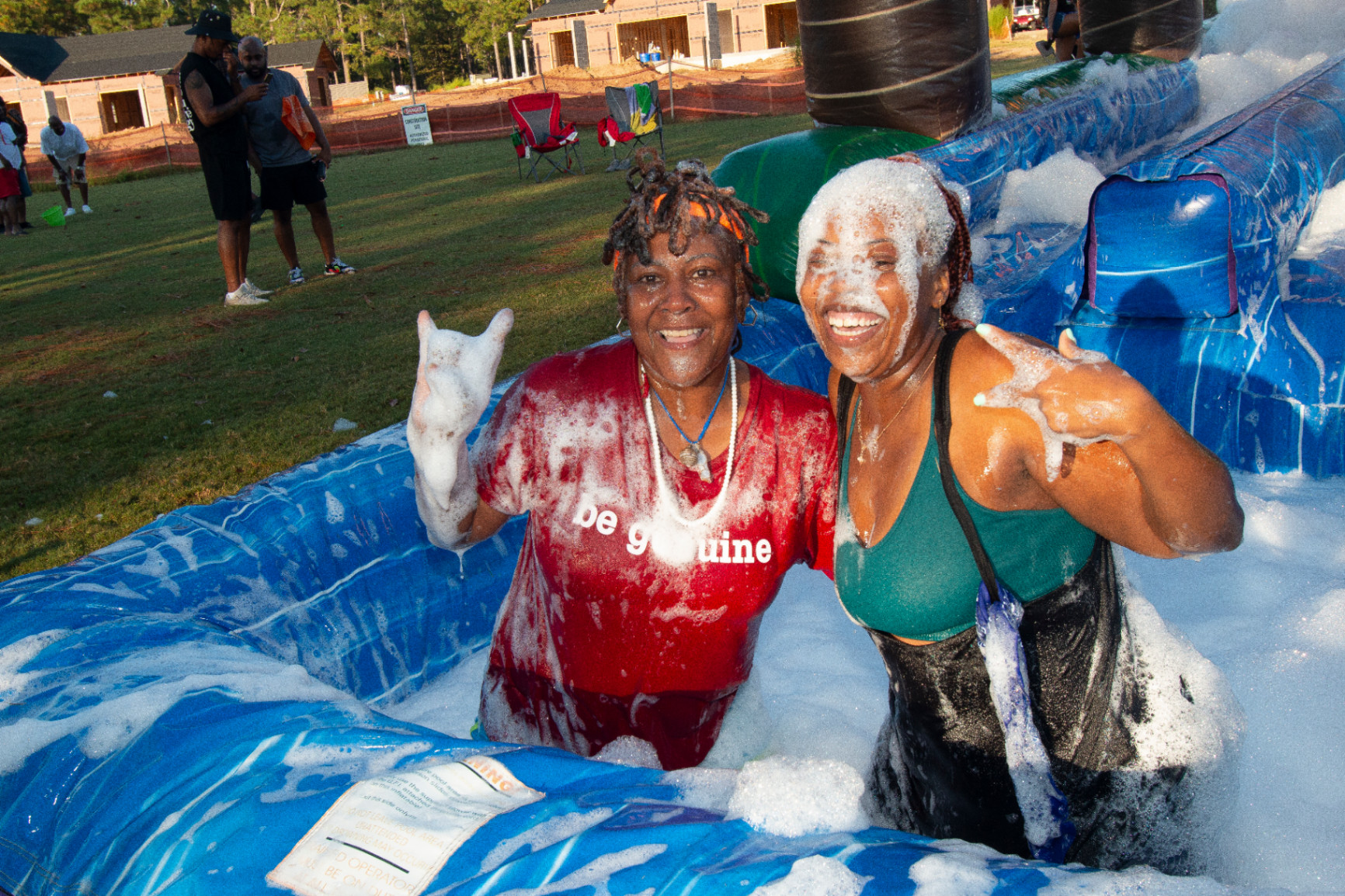 Two women smile and pose in a foam-filled inflatable water slide activity at Melanated Campout