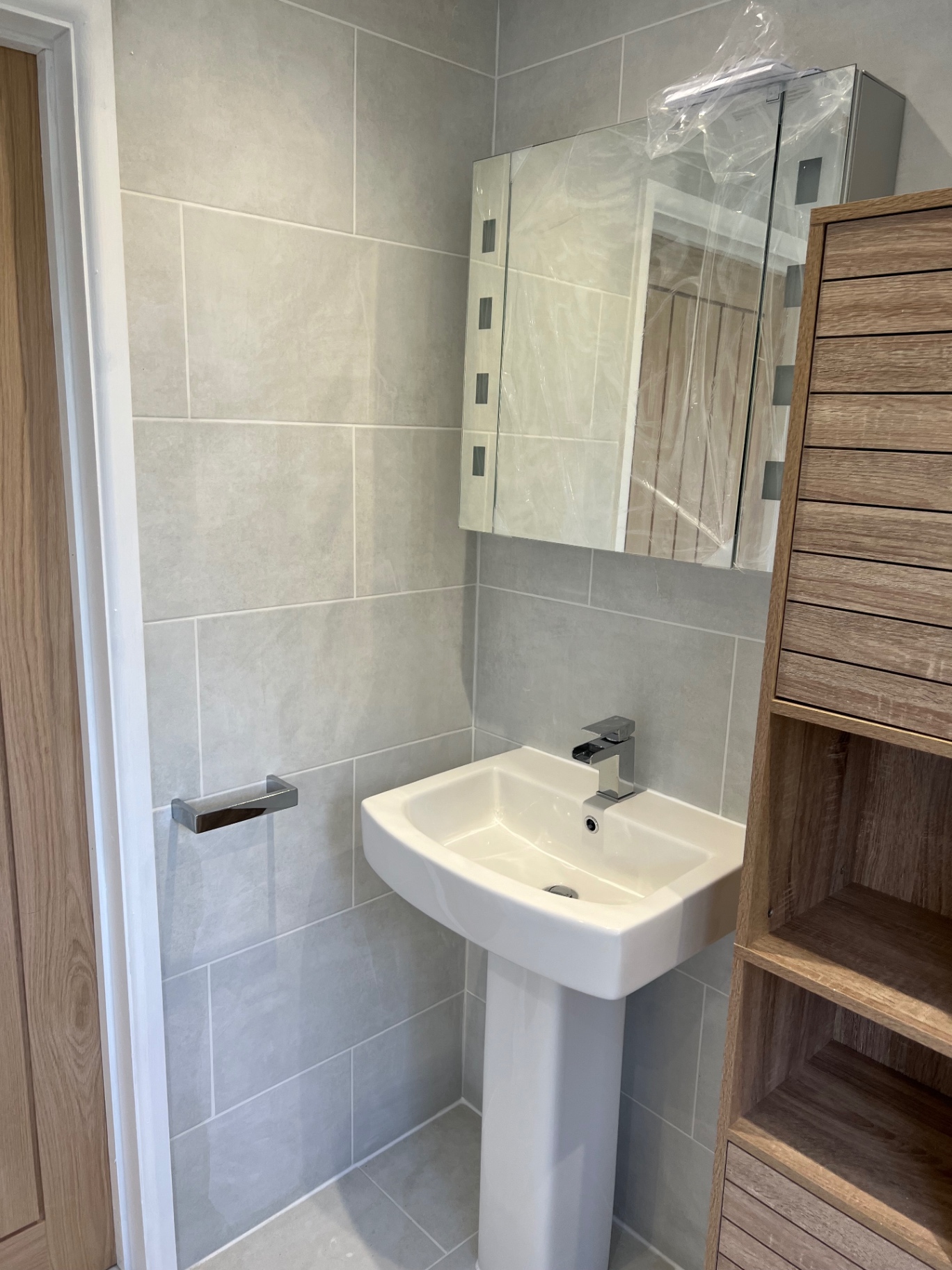Newly installed modern pedestal sink with chrome mixer tap set against eco-friendly light grey tiled walls