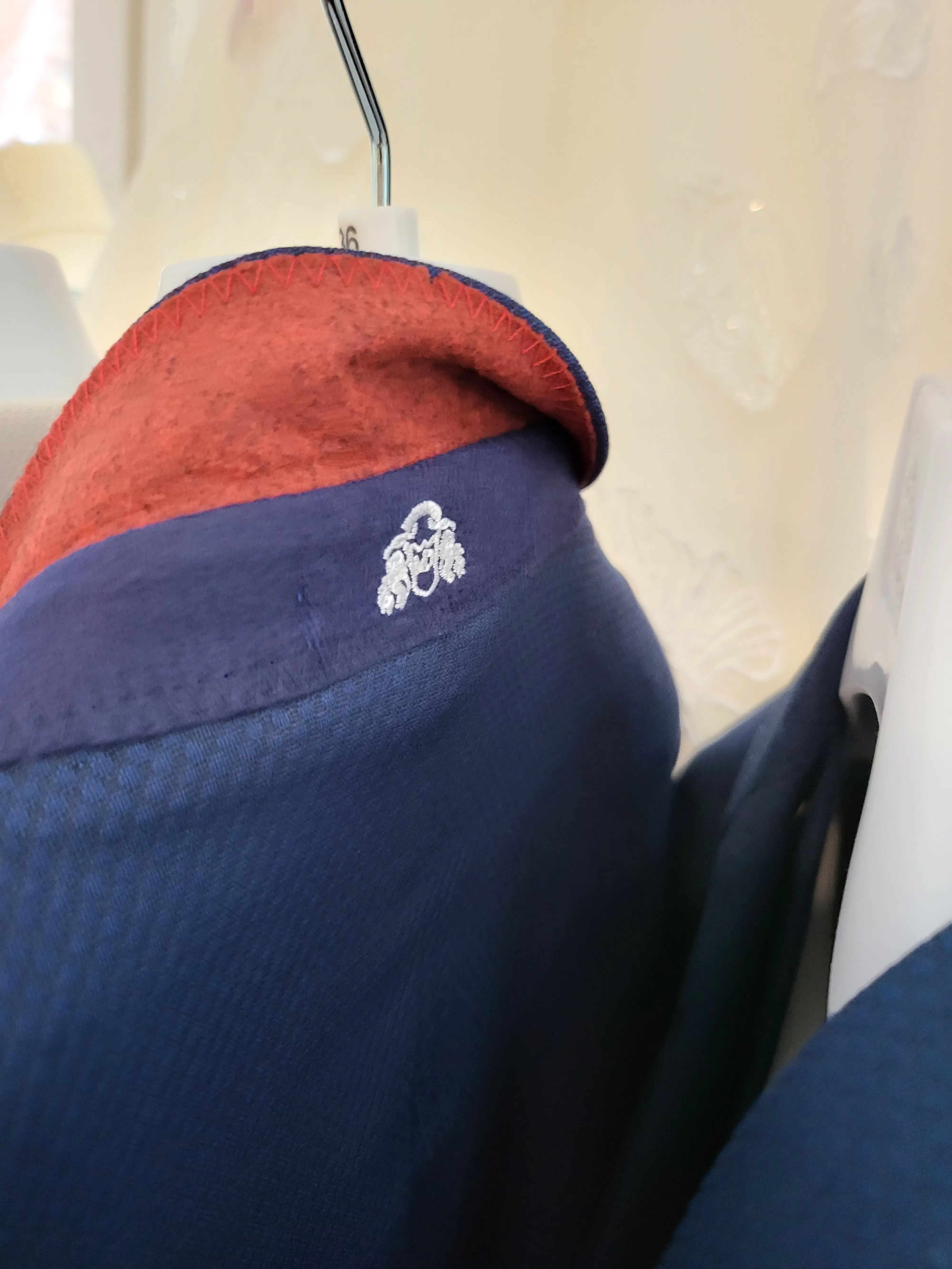 Close-up of a Marc Darcy navy blue men's suit jacket on a hanger, featuring the signature contrasting red velvet undercollar.