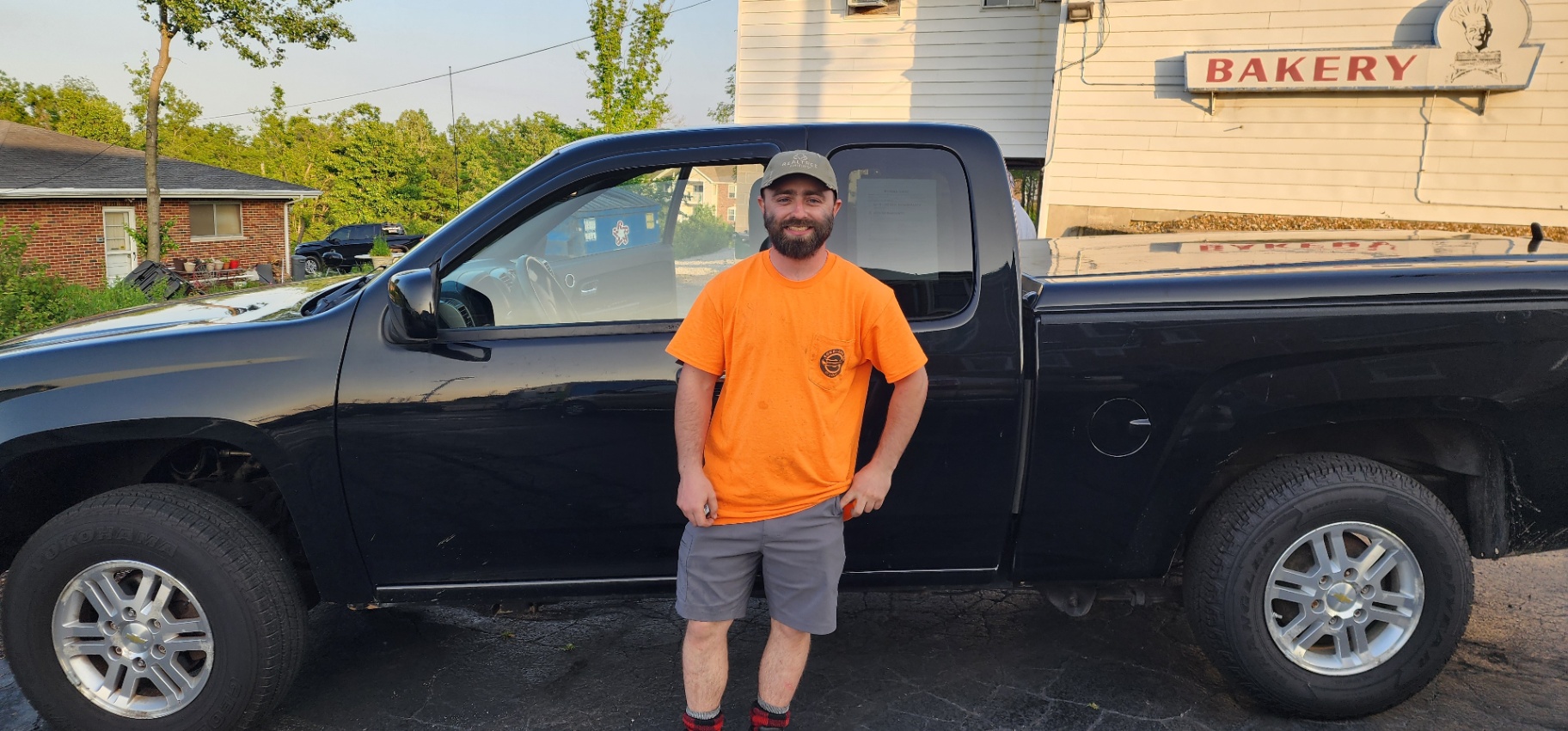 A satisfied Grateful Motors customer stands smiling in front of a clean black pickup truck