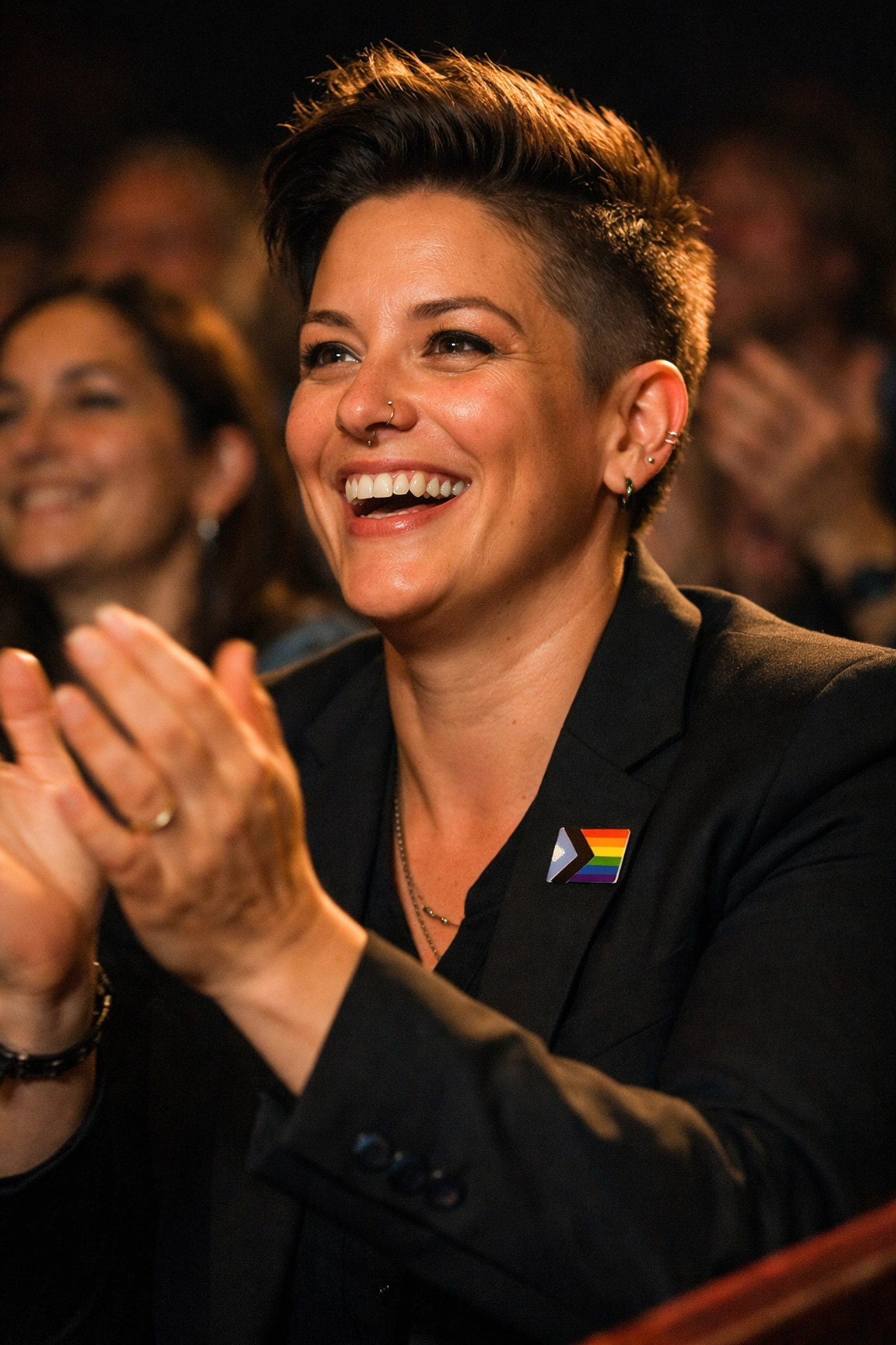 A proud non-binary pibling wearing a pride pin while cheering at a child’s school performance.