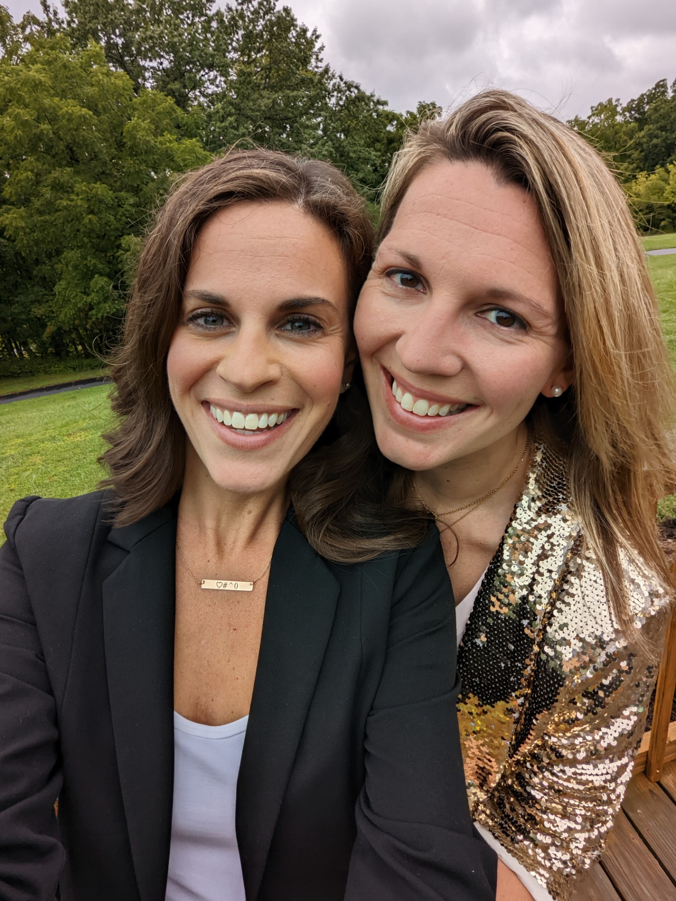 Two women stand close together outdoors, smiling warmly at the camera