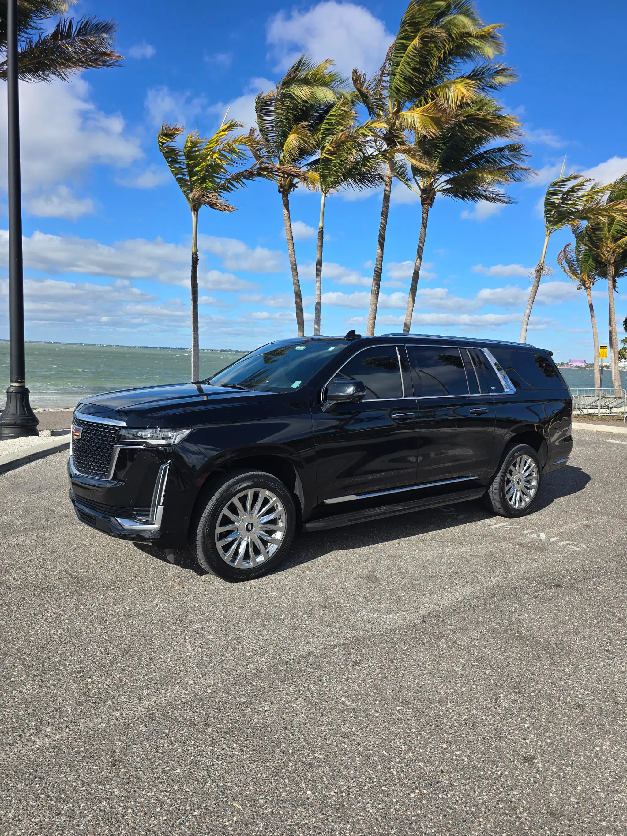 A black Cadillac Escalade ESV from FDJ Luxury Rides parked by the scenic Tampa Bay waterfront.