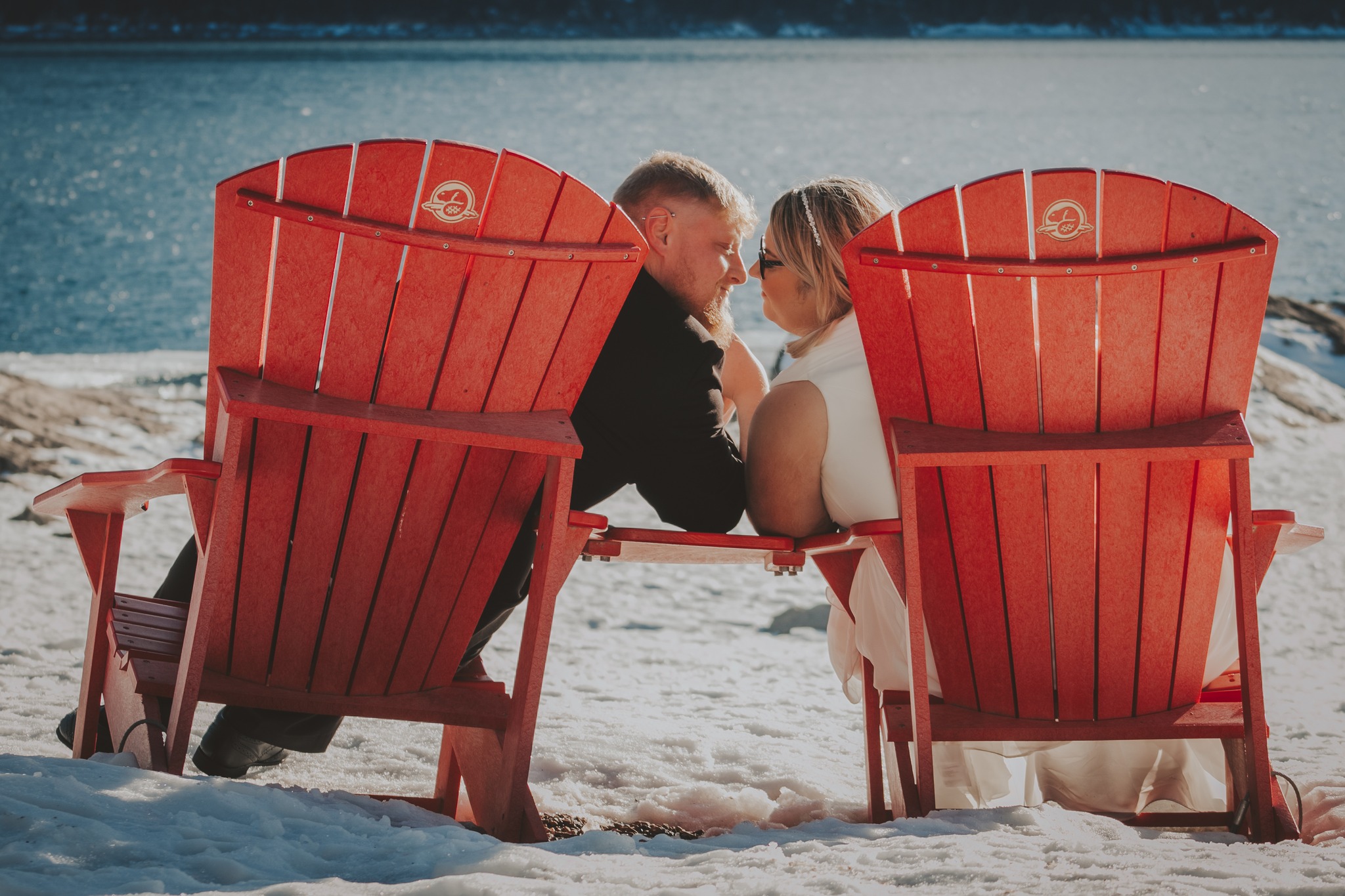 Newly married couple in Adirondack chairs on snowy lakeshore